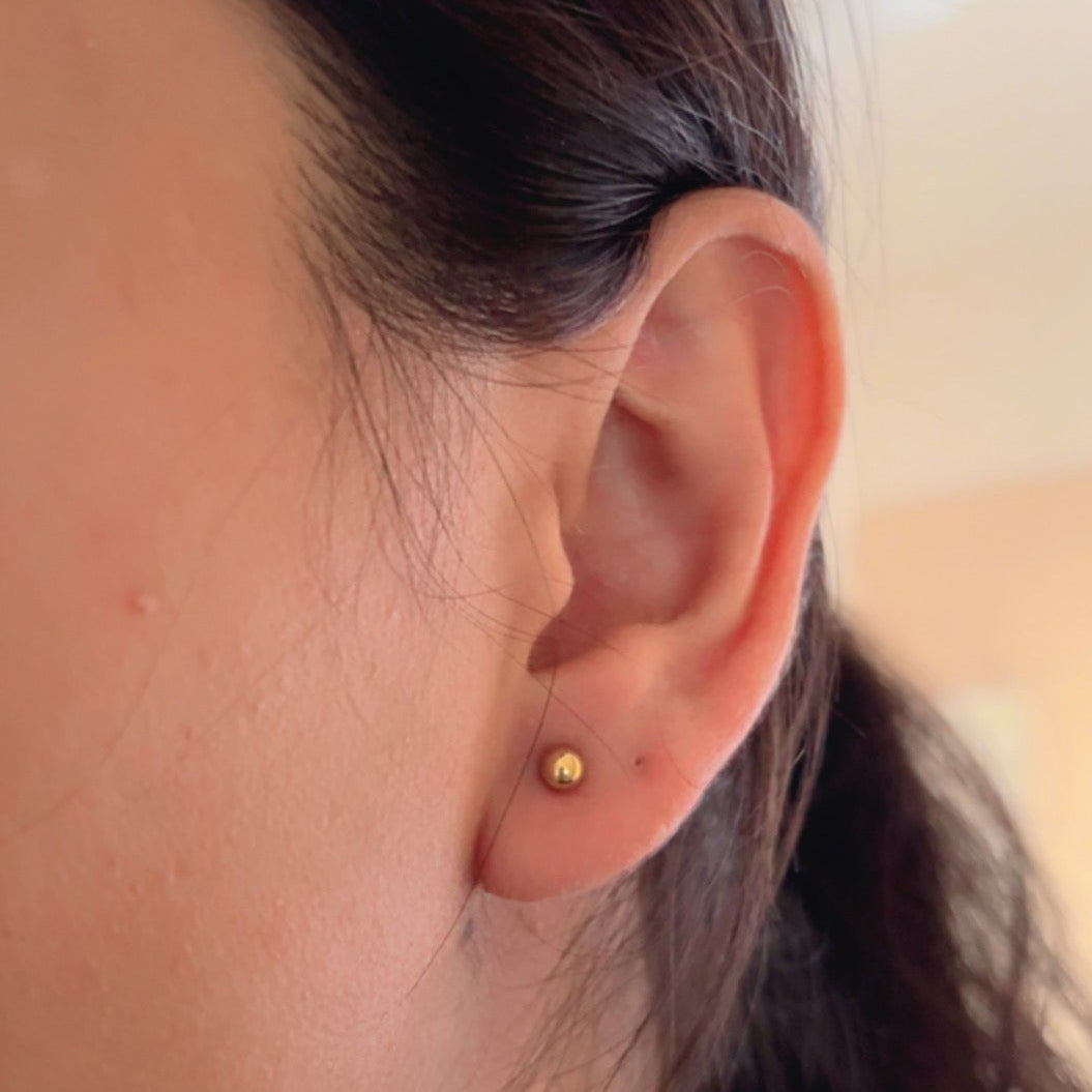 shiny round gold stud earrings placed on neutral background