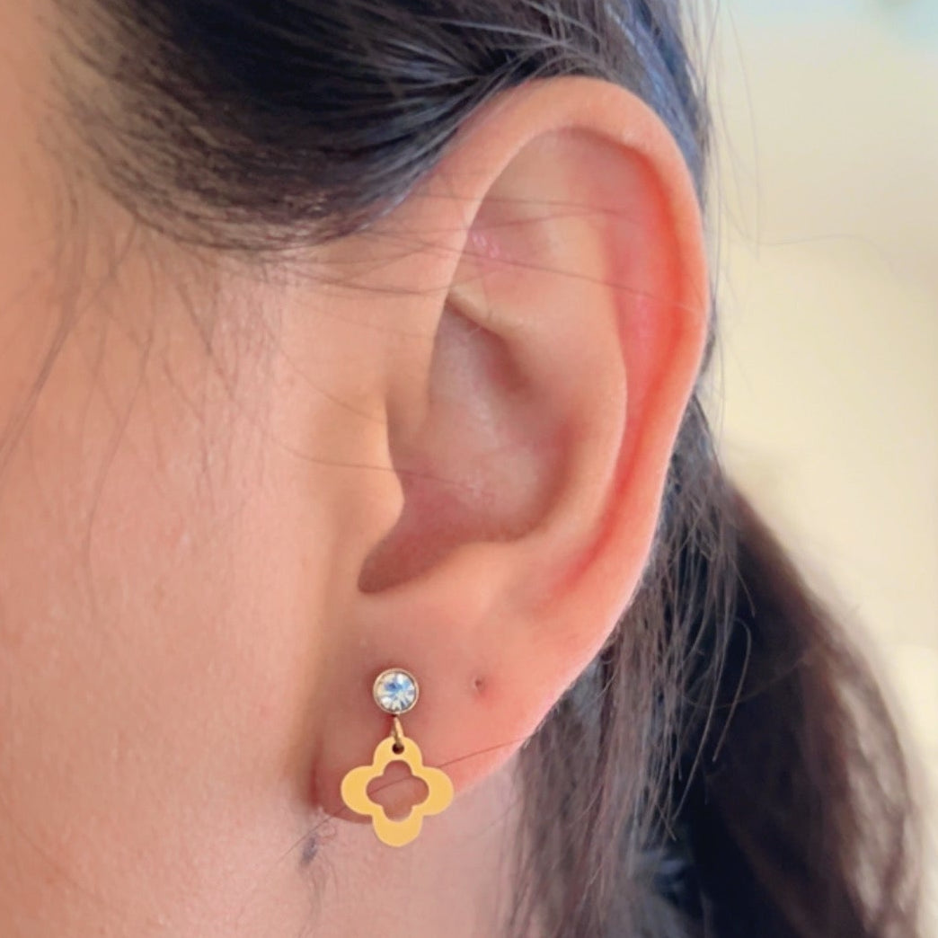 gold earrings with flower charm and crystal stud on soft background