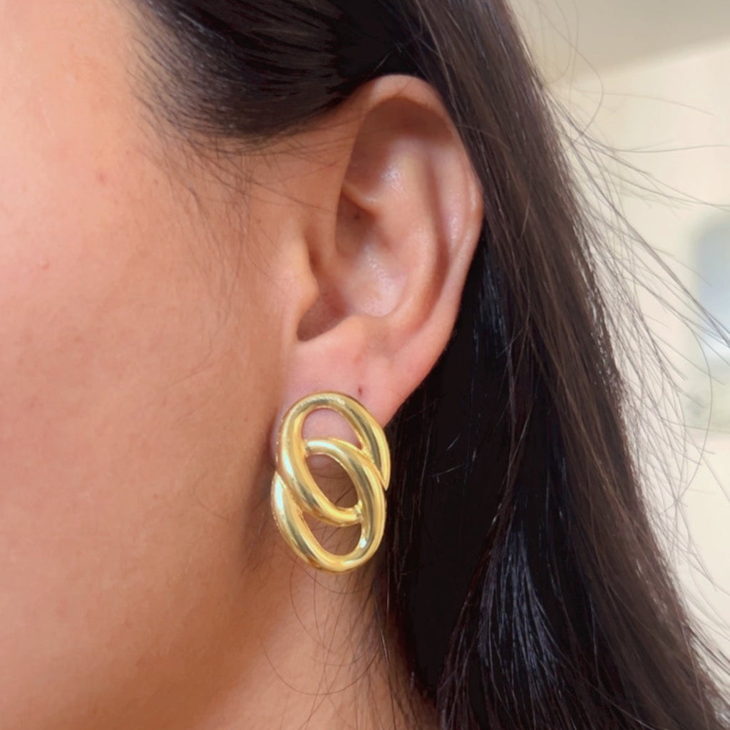 Gold double oval interlocked stud earrings on neutral surface.