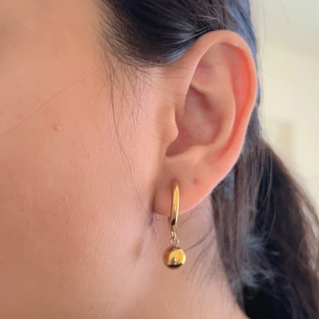 gold hoop earrings with round ball drop design on light background