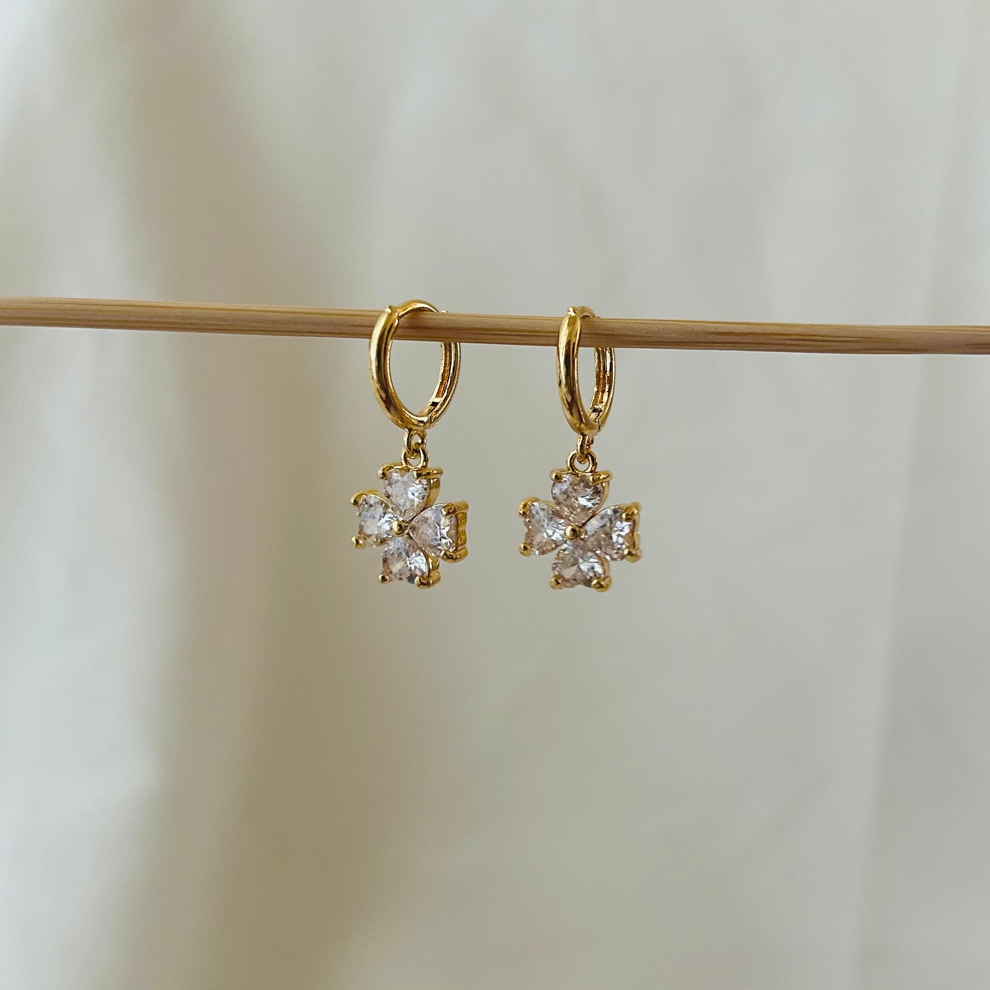 Gold hoop earrings with sparkling flower crystal pendants hanging from a wooden display rod.