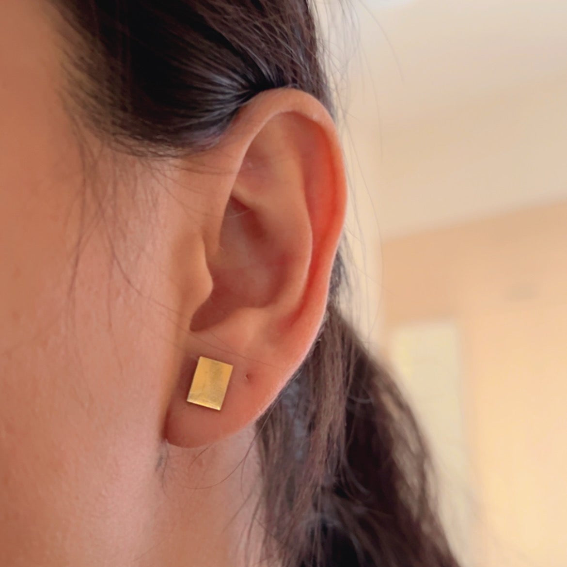 gold square stud earrings with simple geometric design placed on soft neutral background