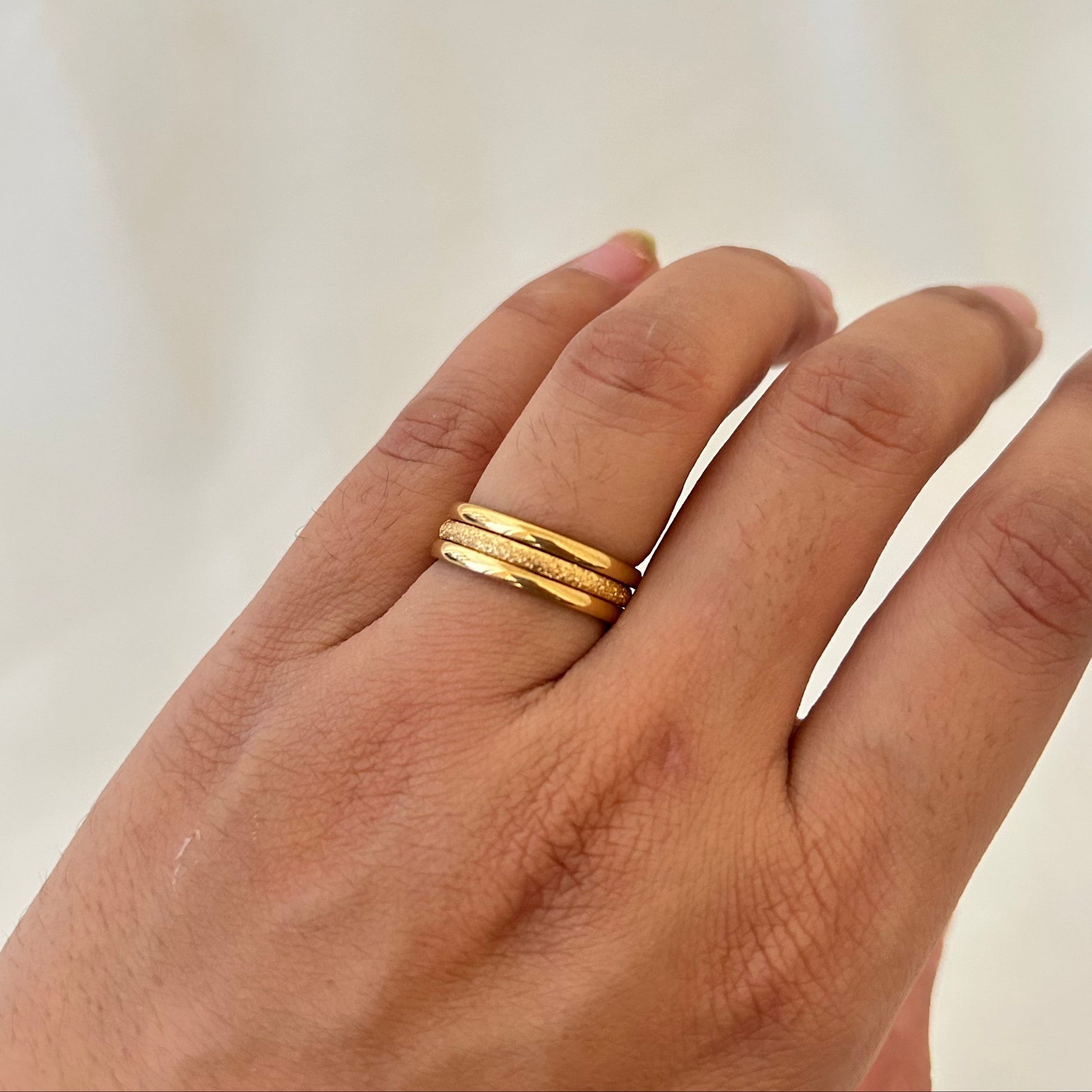 Hand wearing two stacked gold rings with fine textured detailing.