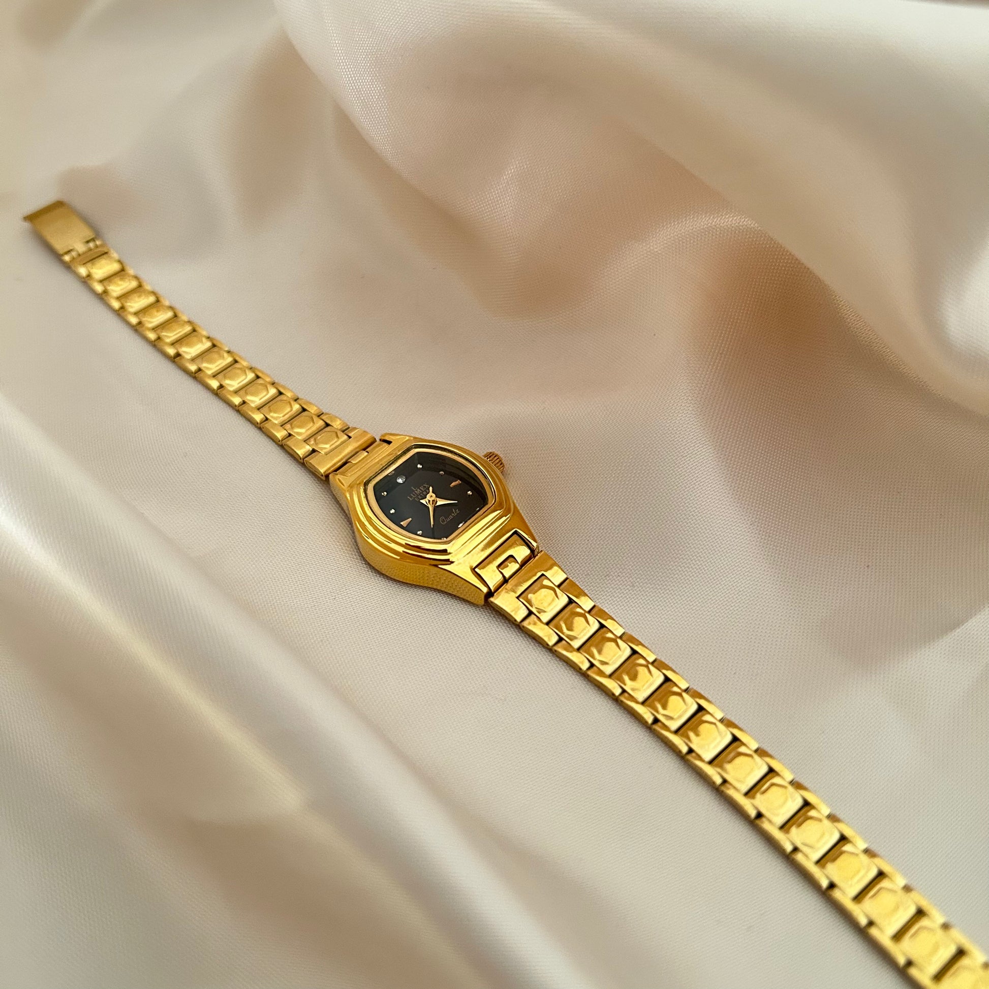 Gold Circle dial wristwatch with linked bracelet placed on soft beige satin background, elegant minimal design.