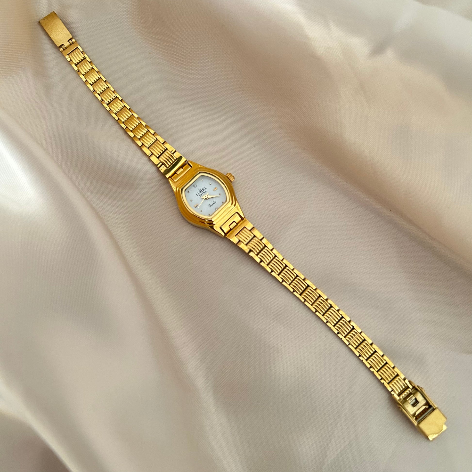 Gold Circle dial wristwatch with linked bracelet placed on soft beige satin background, elegant minimal design.