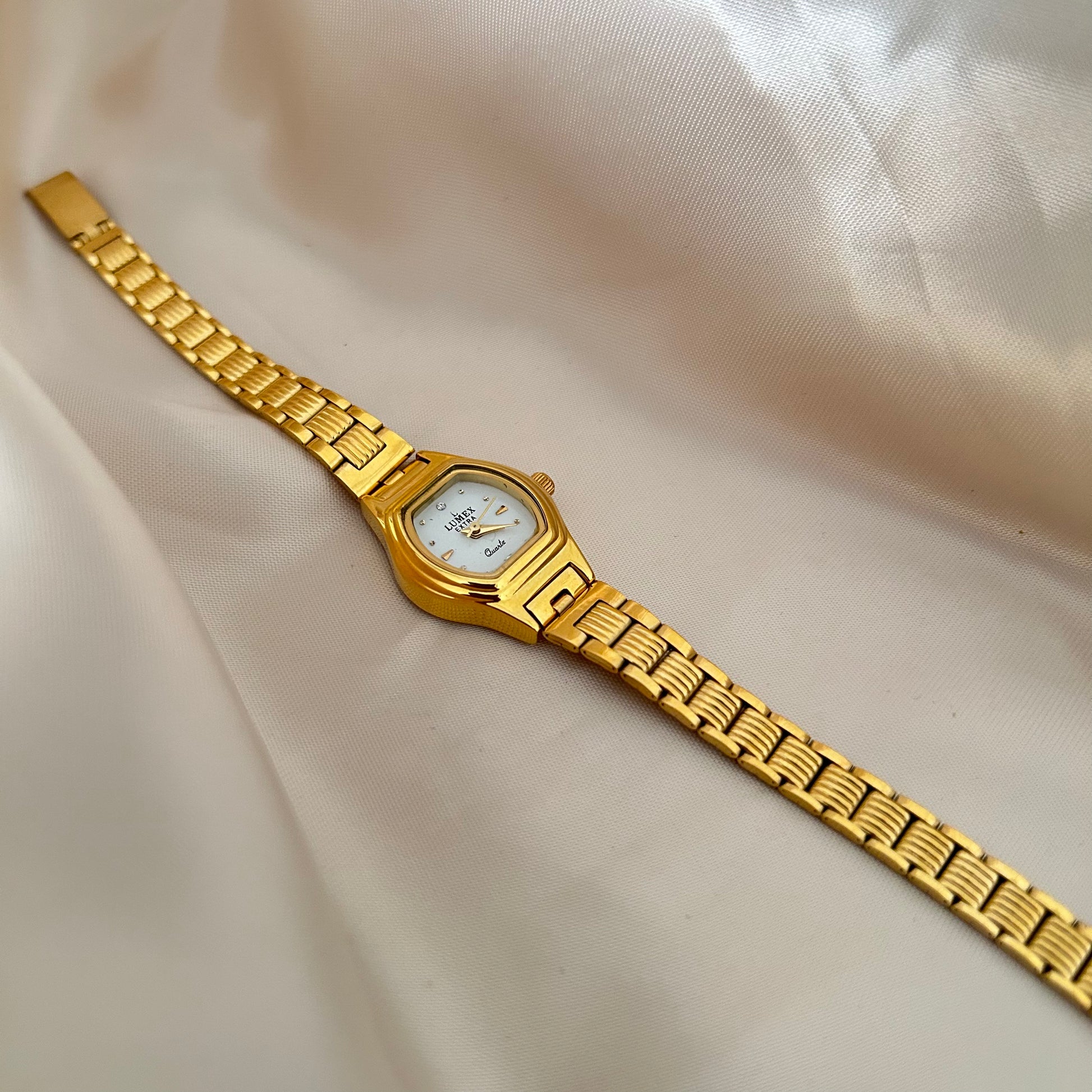 Gold Circle dial wristwatch with linked bracelet placed on soft beige satin background, elegant minimal design.