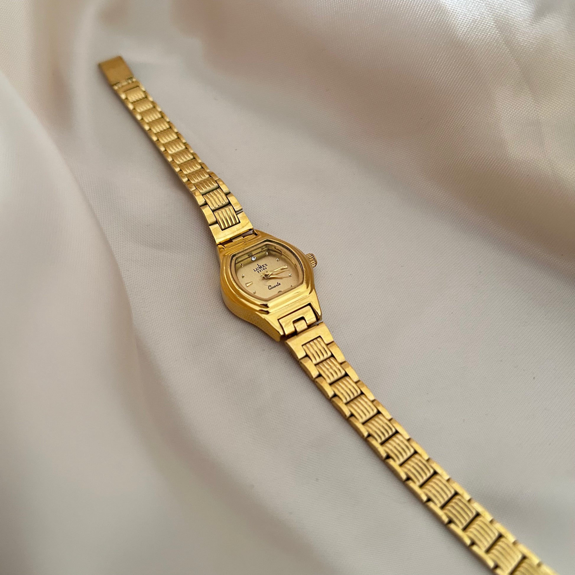 Gold Circle dial wristwatch with linked bracelet placed on soft beige satin background, elegant minimal design.