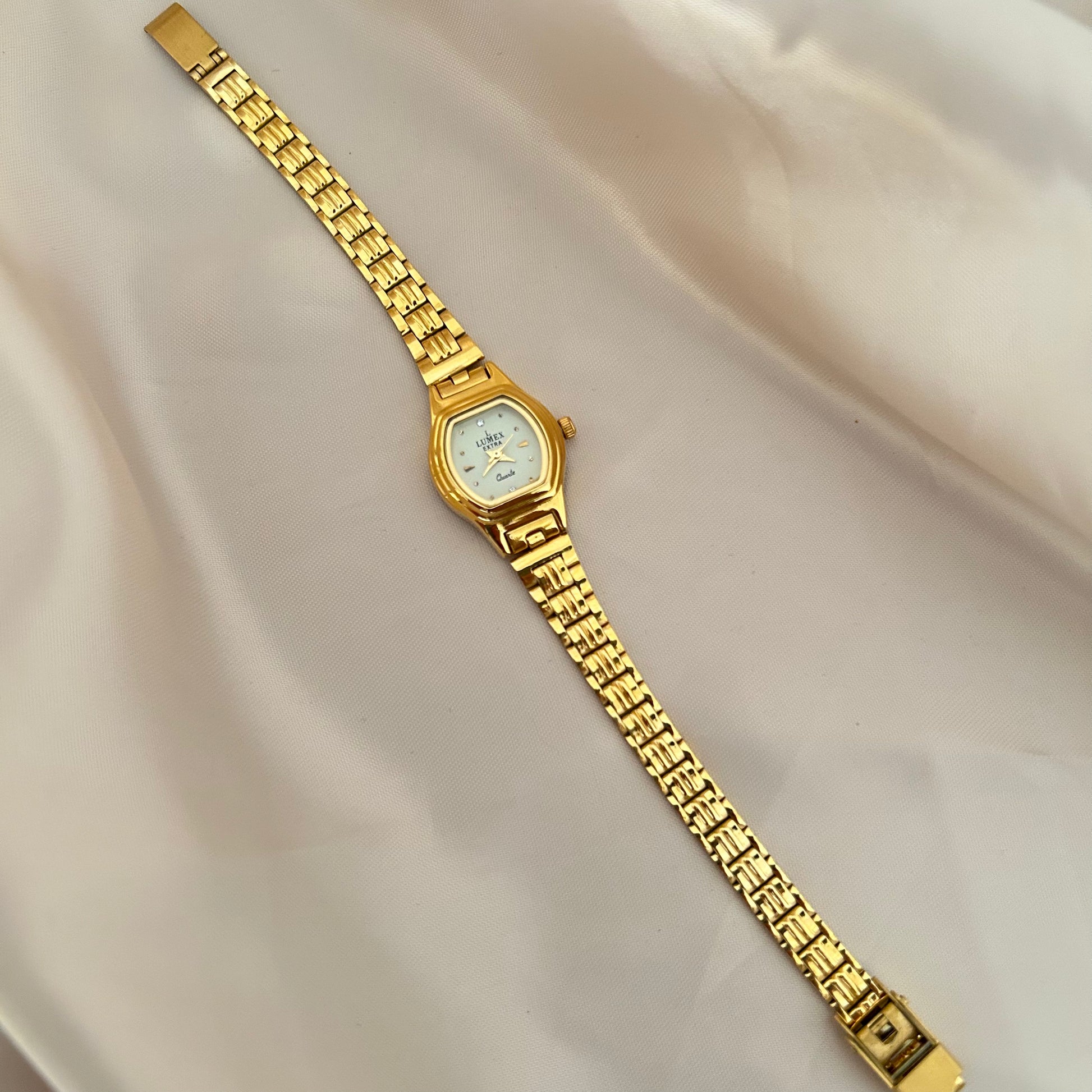 Gold Circle dial wristwatch with linked bracelet placed on soft beige satin background, elegant minimal design.