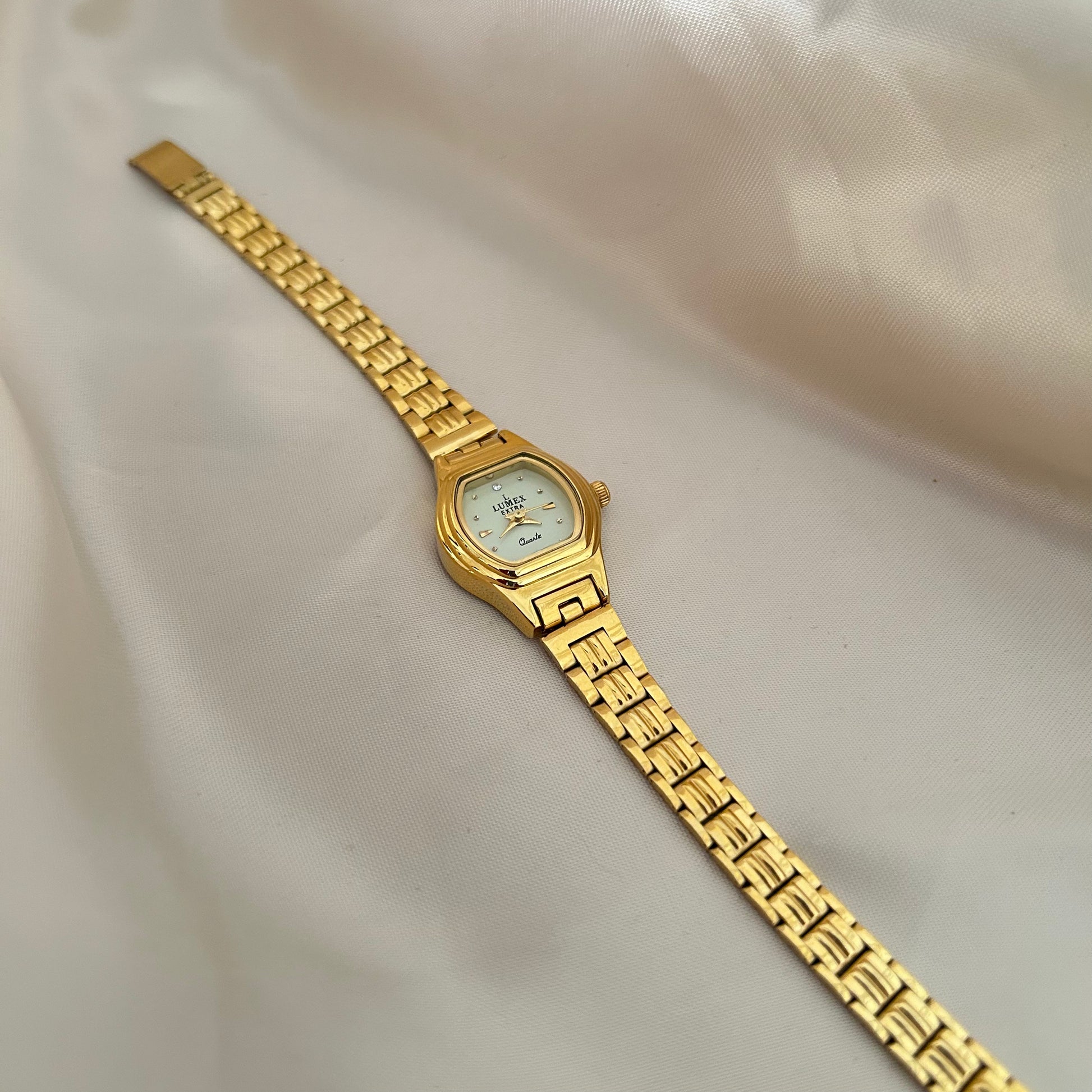 Gold Circle dial wristwatch with linked bracelet placed on soft beige satin background, elegant minimal design.