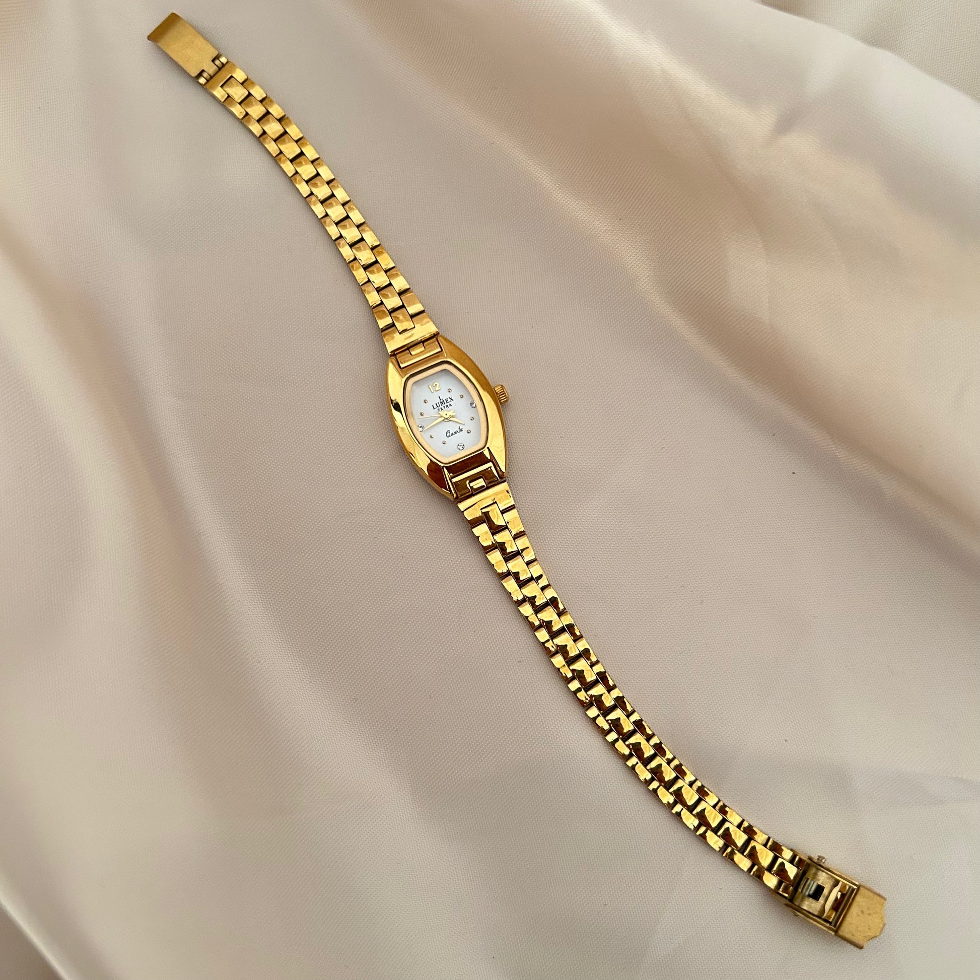 Gold oval dial wristwatch with linked bracelet placed on soft beige satin background, elegant minimal design.