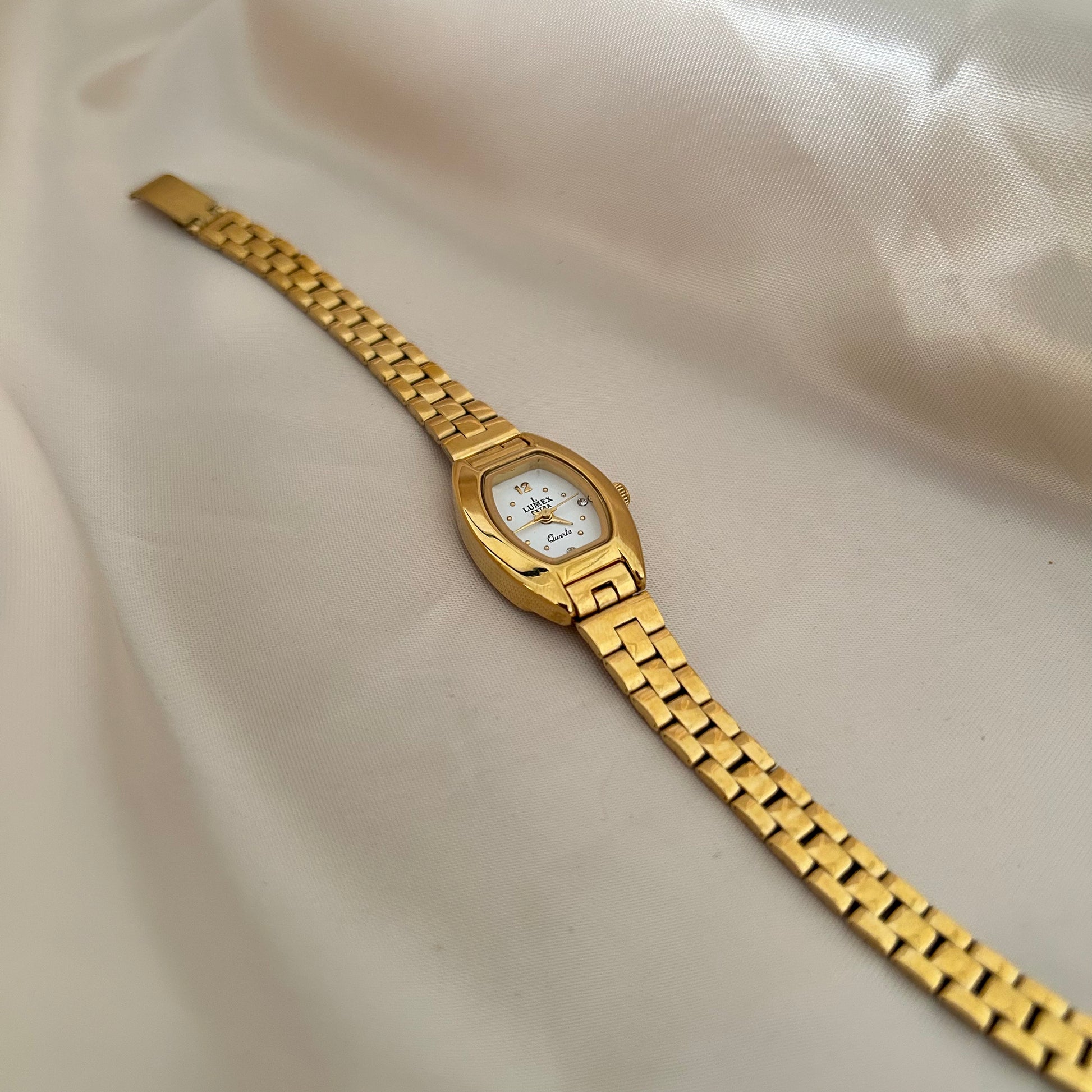 Gold oval dial wristwatch with linked bracelet placed on soft beige satin background, elegant minimal design.
