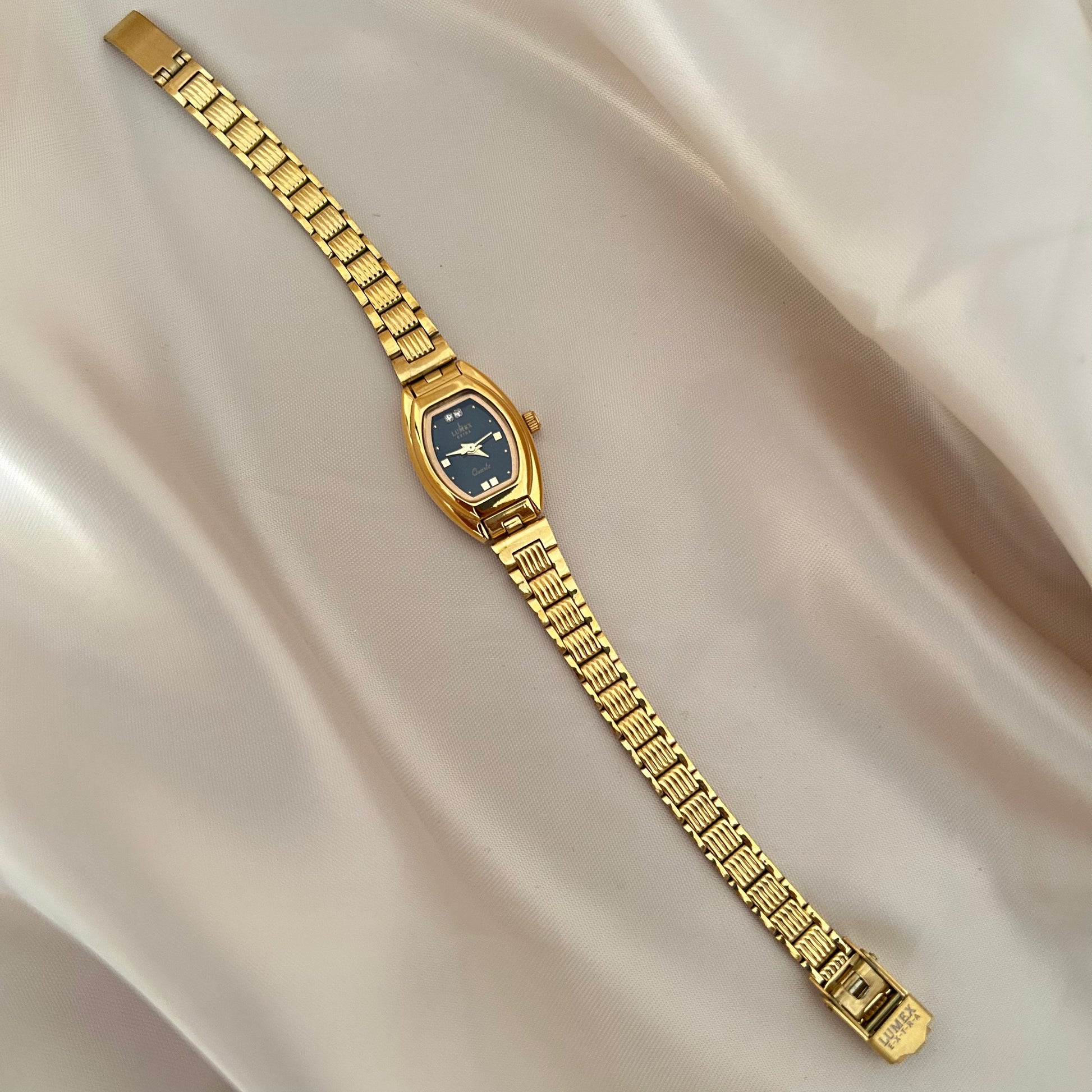 Gold oval dial wristwatch with linked bracelet placed on soft beige satin background, elegant minimal design.