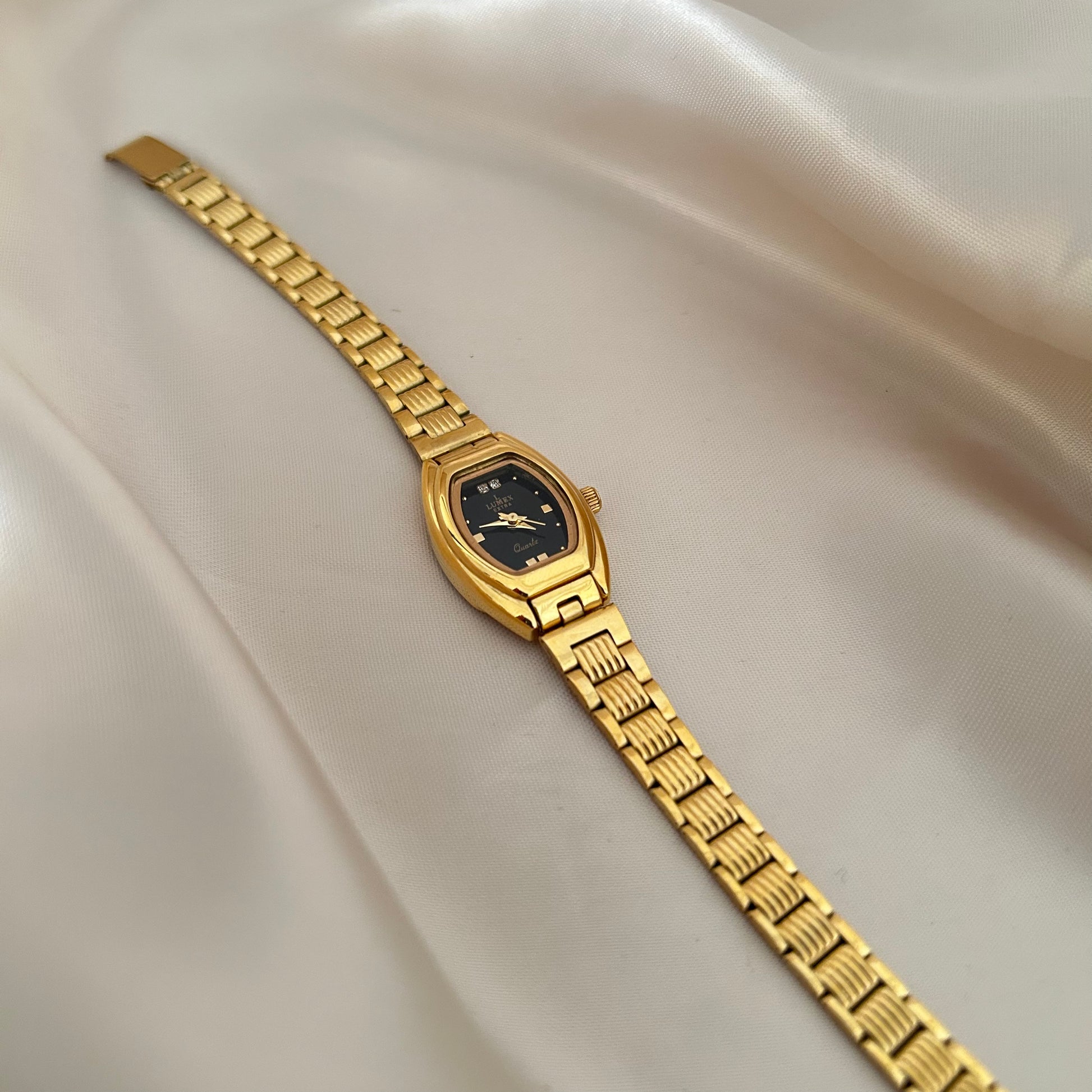 Gold oval dial wristwatch with linked bracelet placed on soft beige satin background, elegant minimal design.