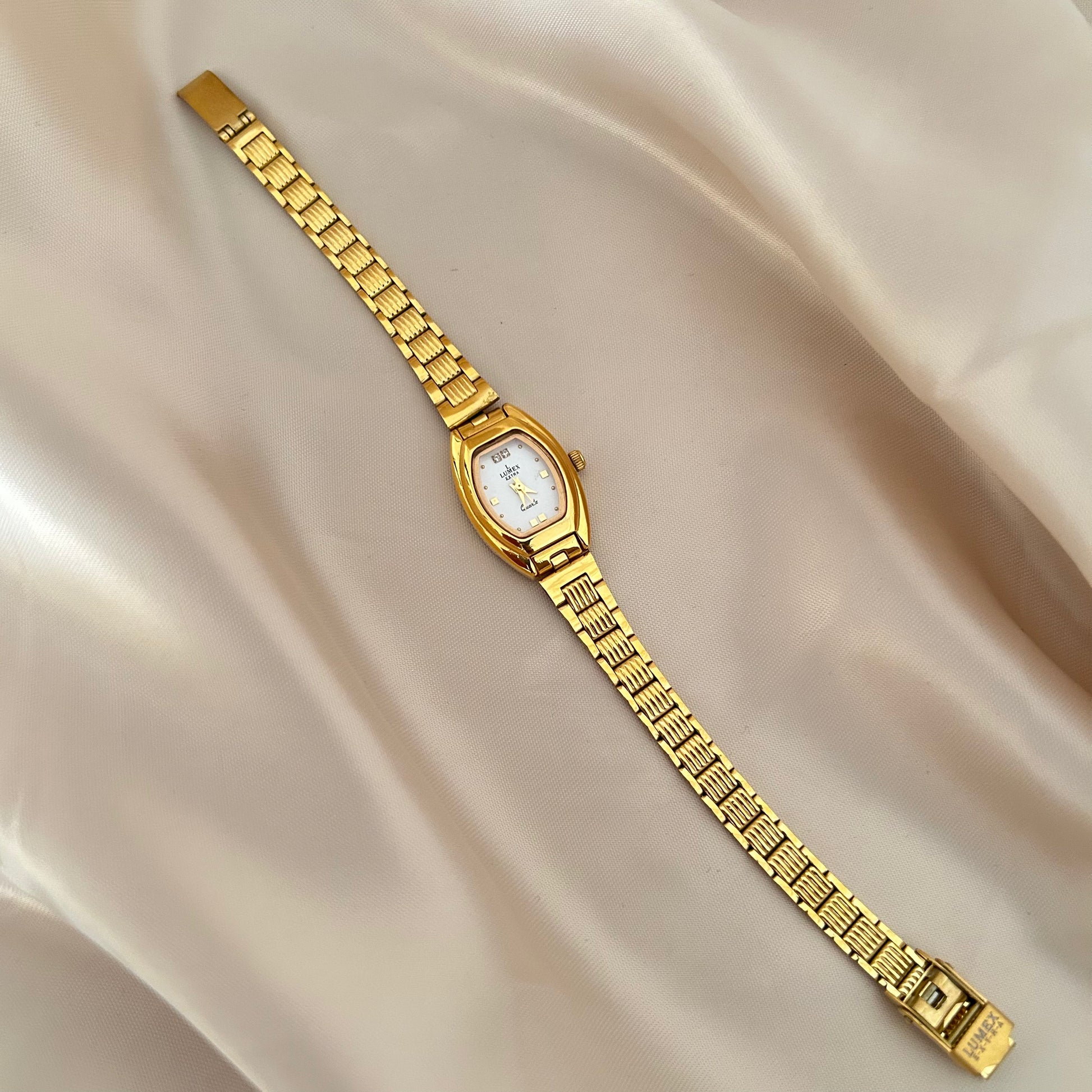 Gold oval dial wristwatch with linked bracelet placed on soft beige satin background, elegant minimal design.