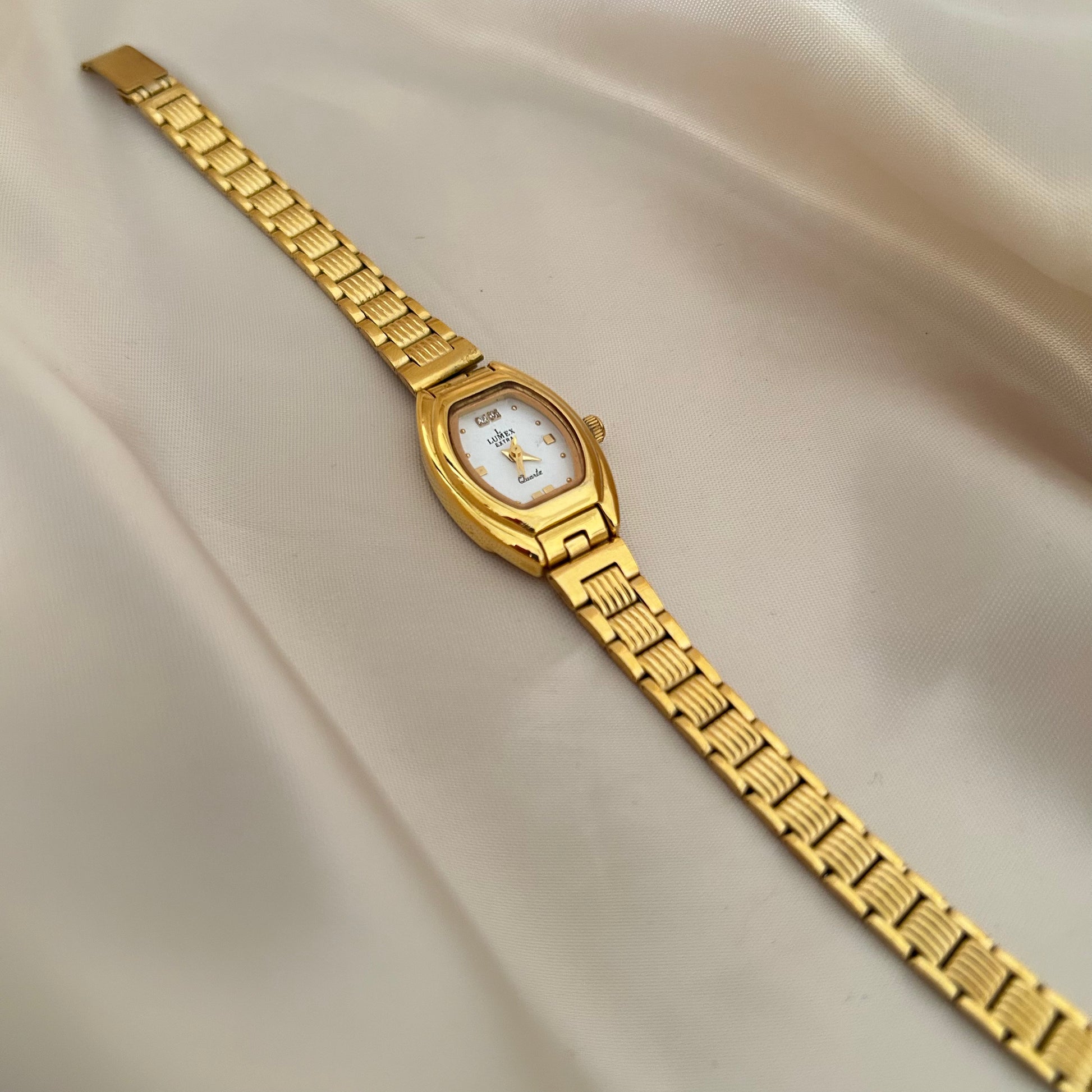 Gold oval dial wristwatch with linked bracelet placed on soft beige satin background, elegant minimal design.