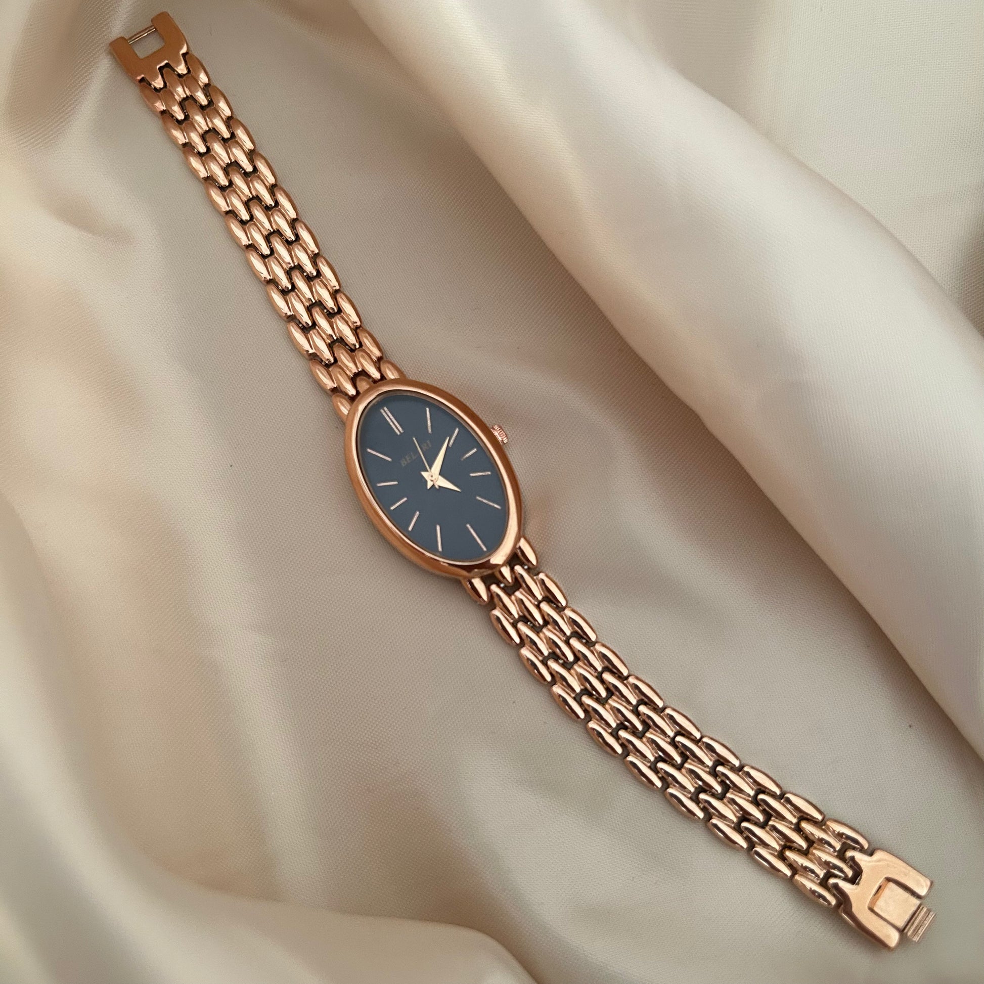 Rose gold wristwatch with black dial and metal strap on soft satin background.