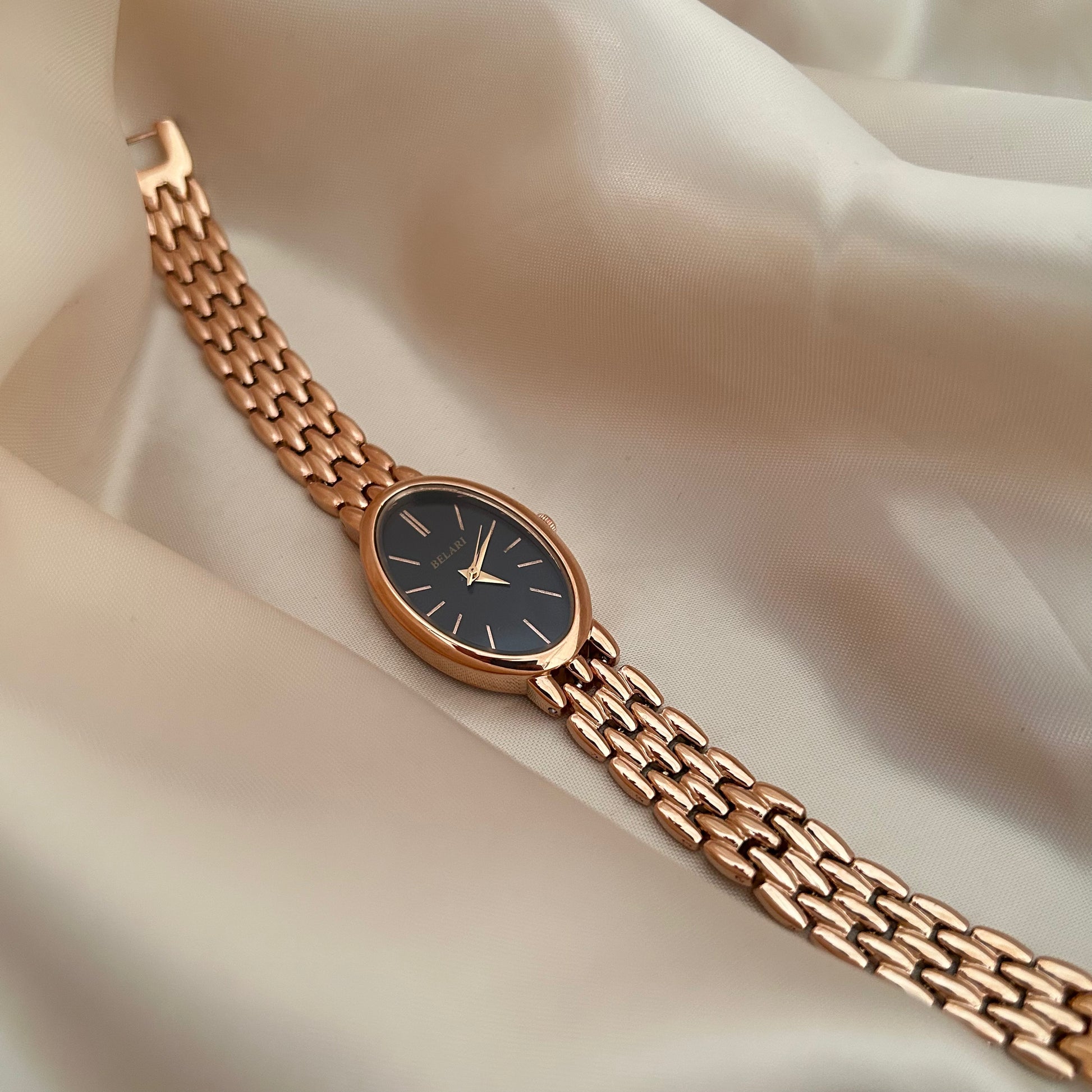 Rose gold wristwatch with black dial and metal strap on soft satin background.