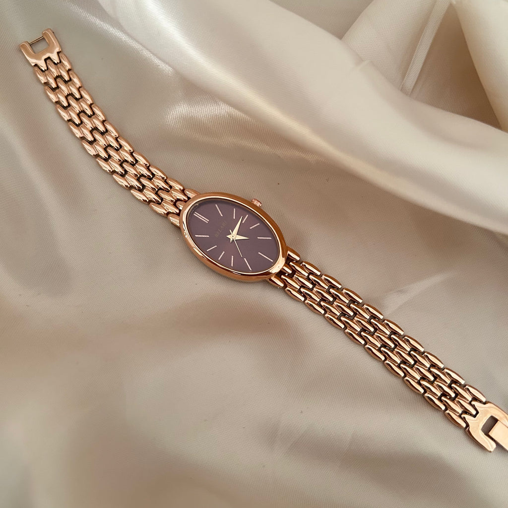 Rose gold wristwatch with Megentta dial and metal strap on soft satin background.