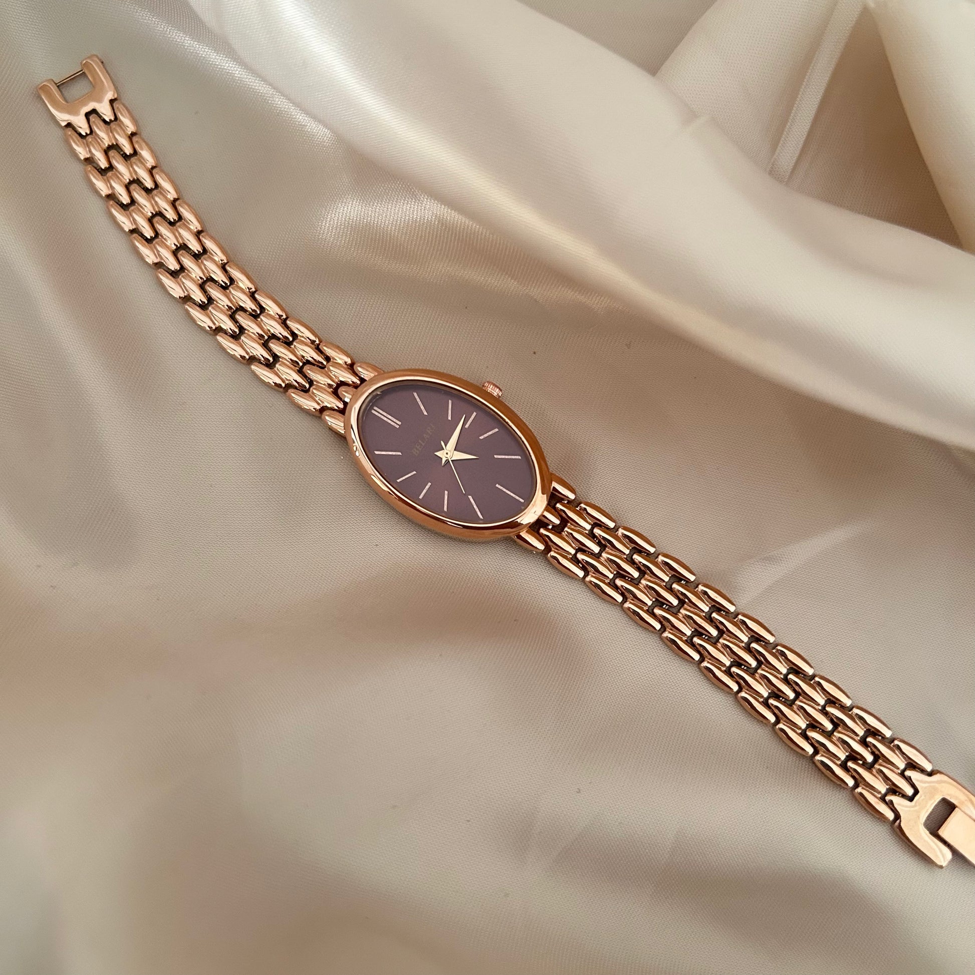 Rose gold wristwatch with Megentta dial and metal strap on soft satin background.