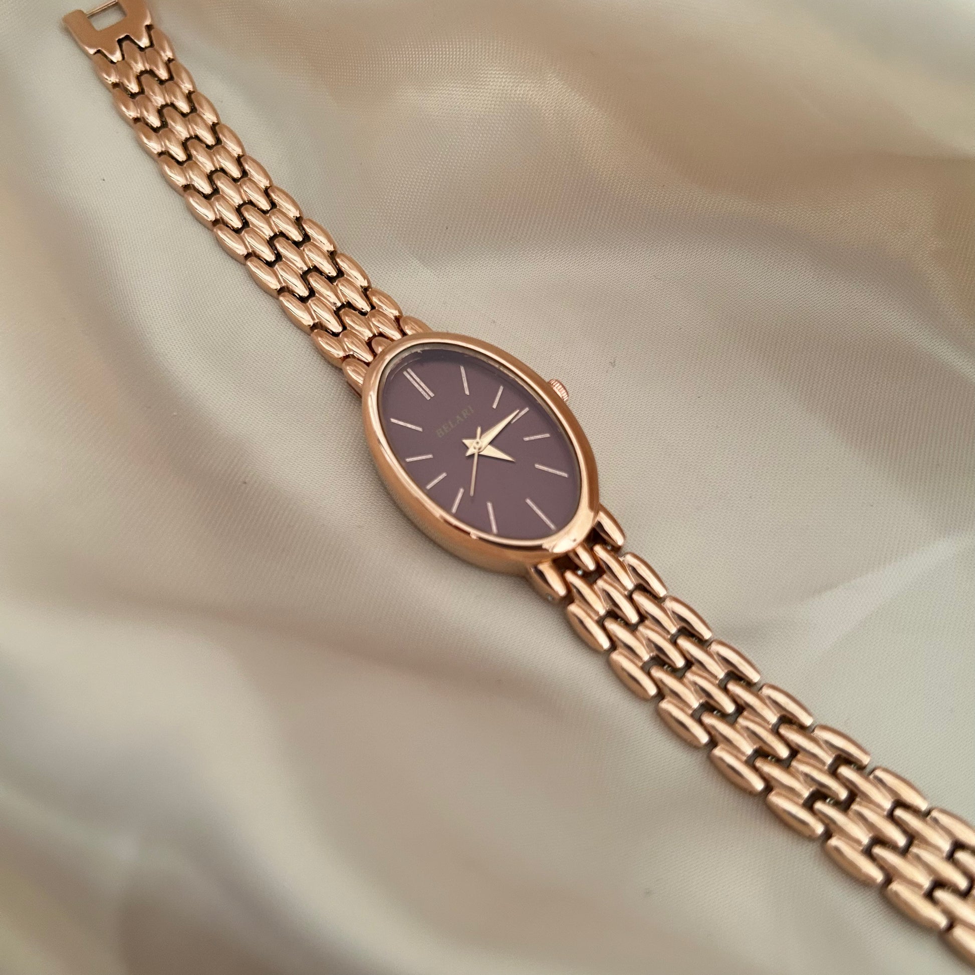 Rose gold wristwatch with Megentta dial and metal strap on soft satin background.