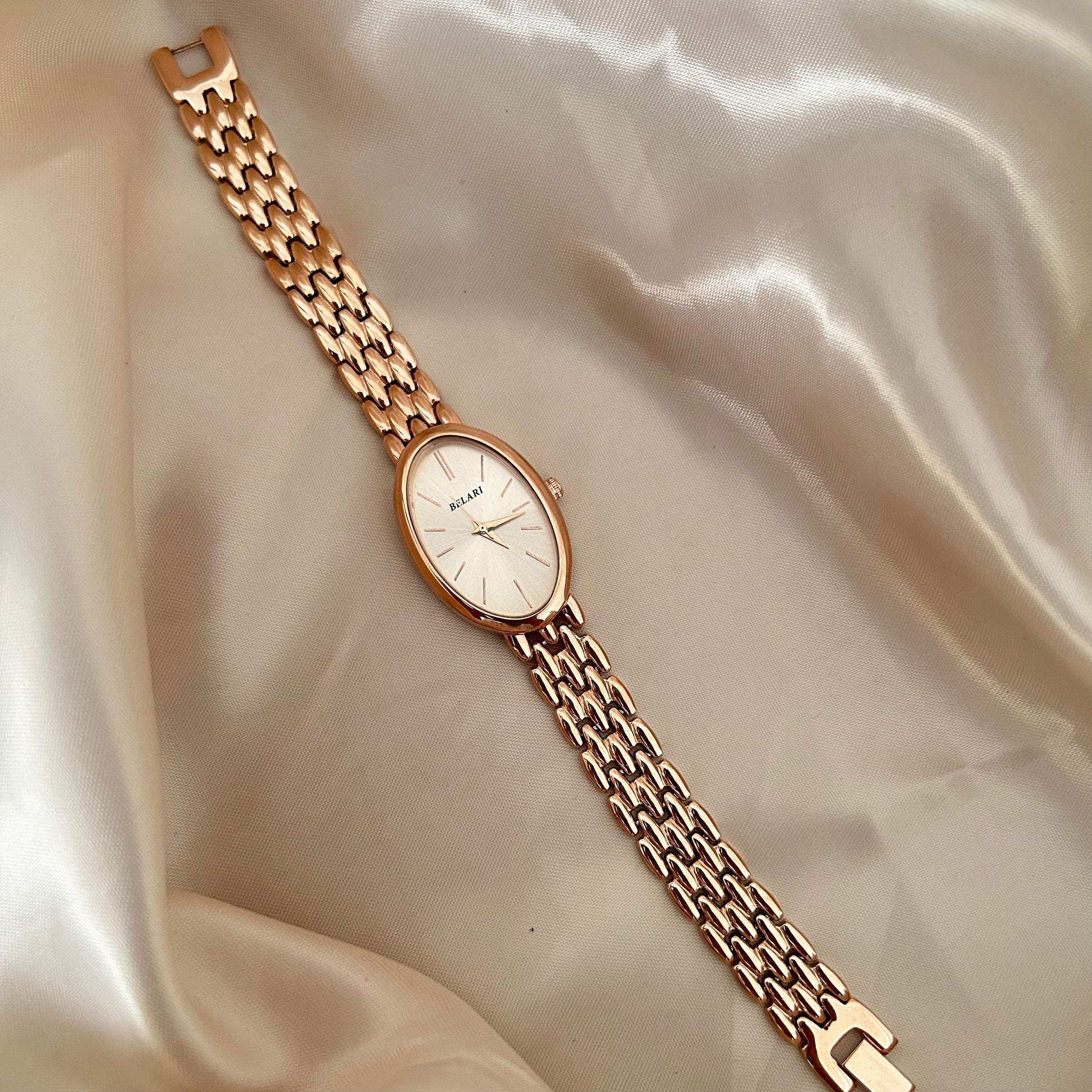 Rose gold wristwatch with Rose gold dial and metal strap on soft satin background.