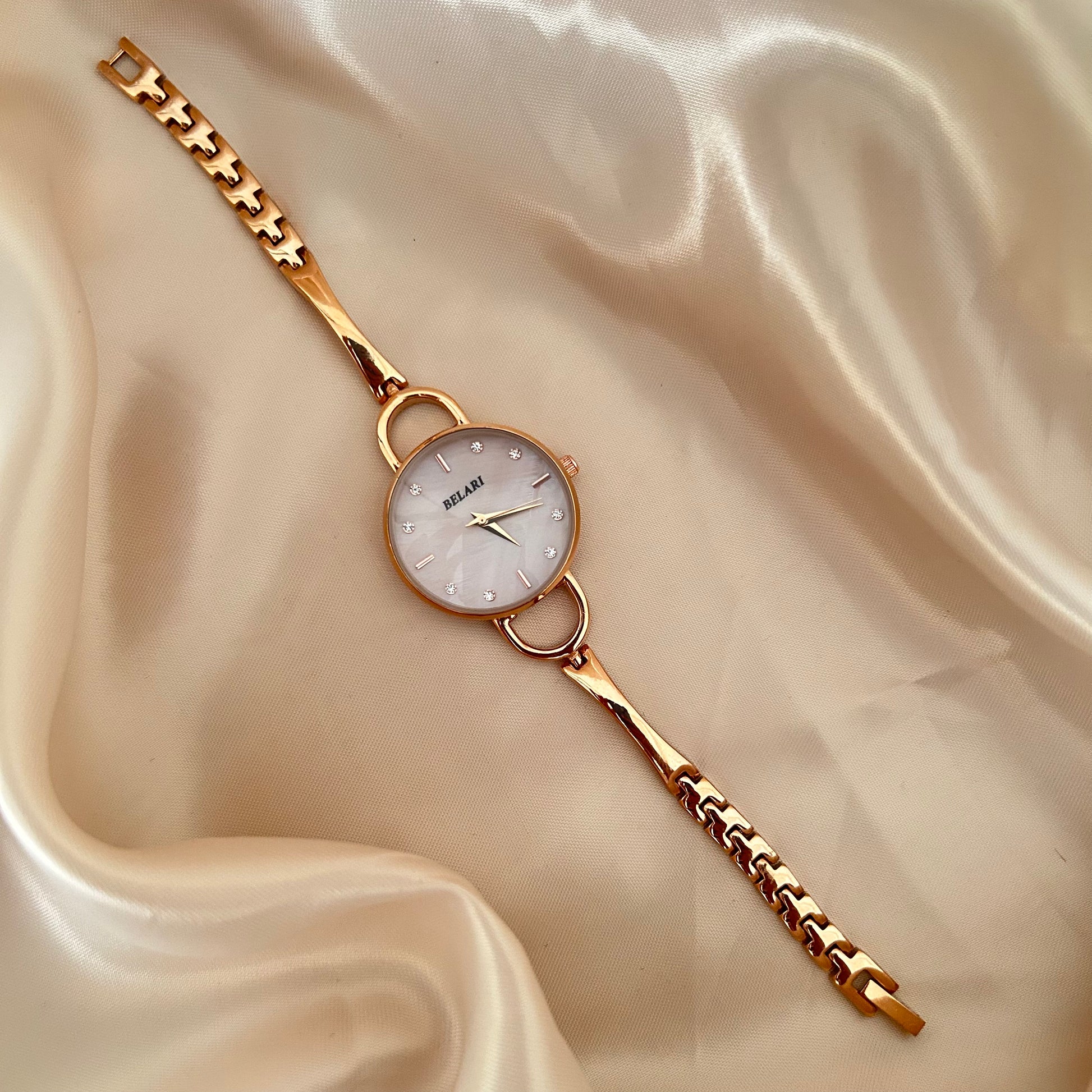 Slim gold wristwatch with loop connectors and small dial on beige satin background.