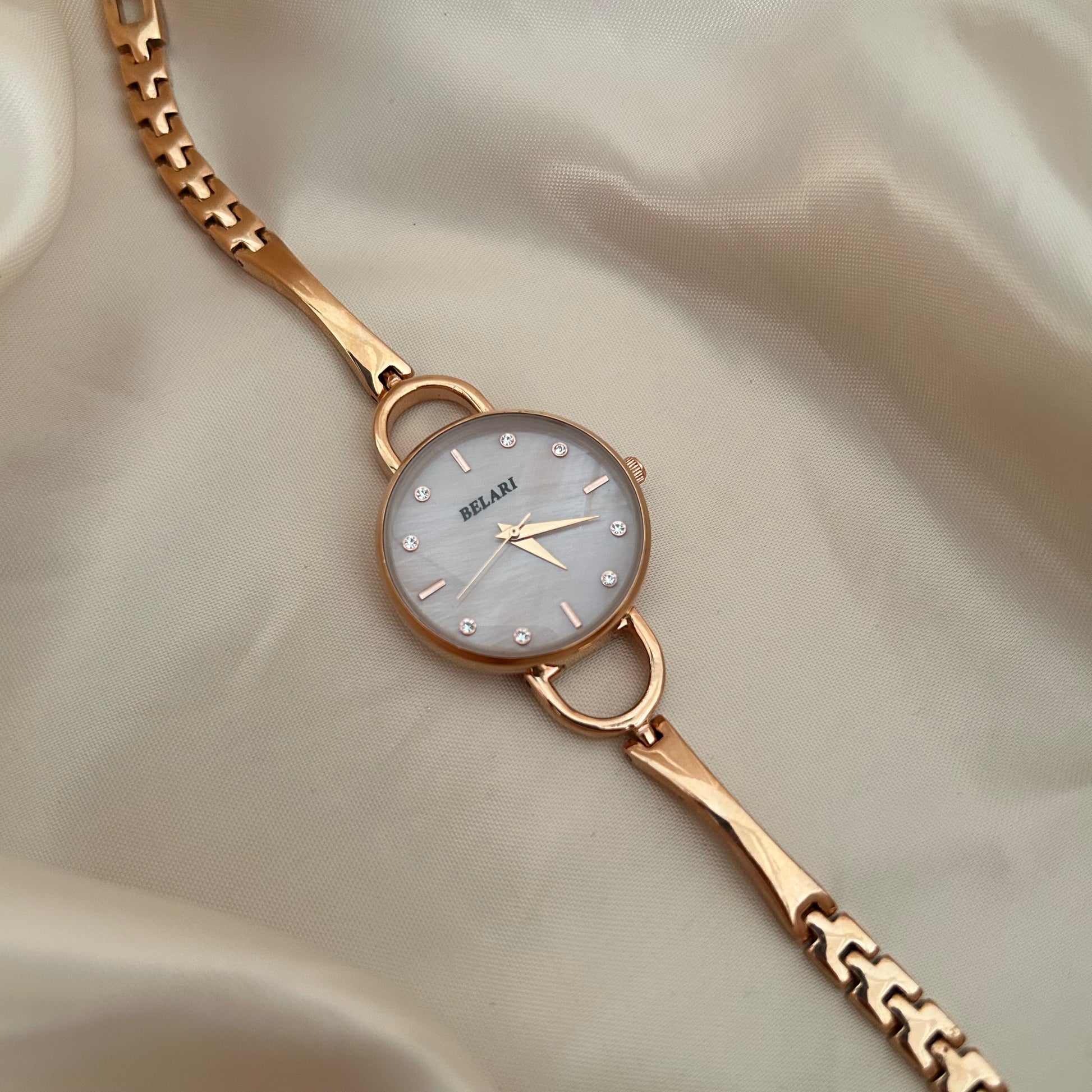 Slim gold wristwatch with loop connectors and small dial on beige satin background.