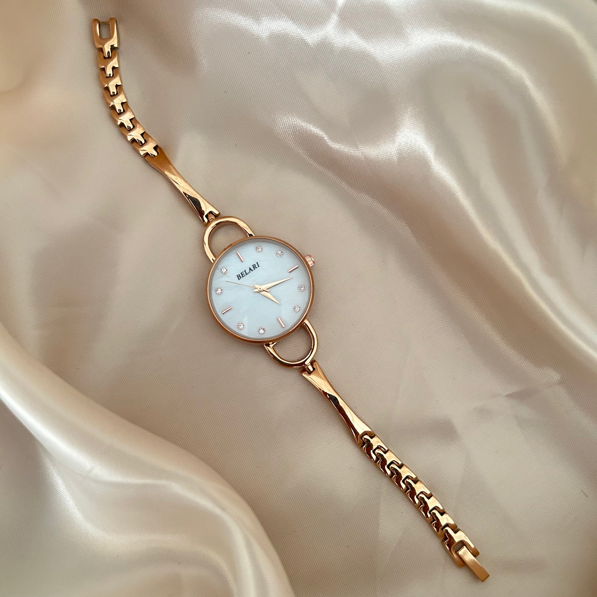 Slim gold wristwatch with loop connectors and small dial on beige satin background.