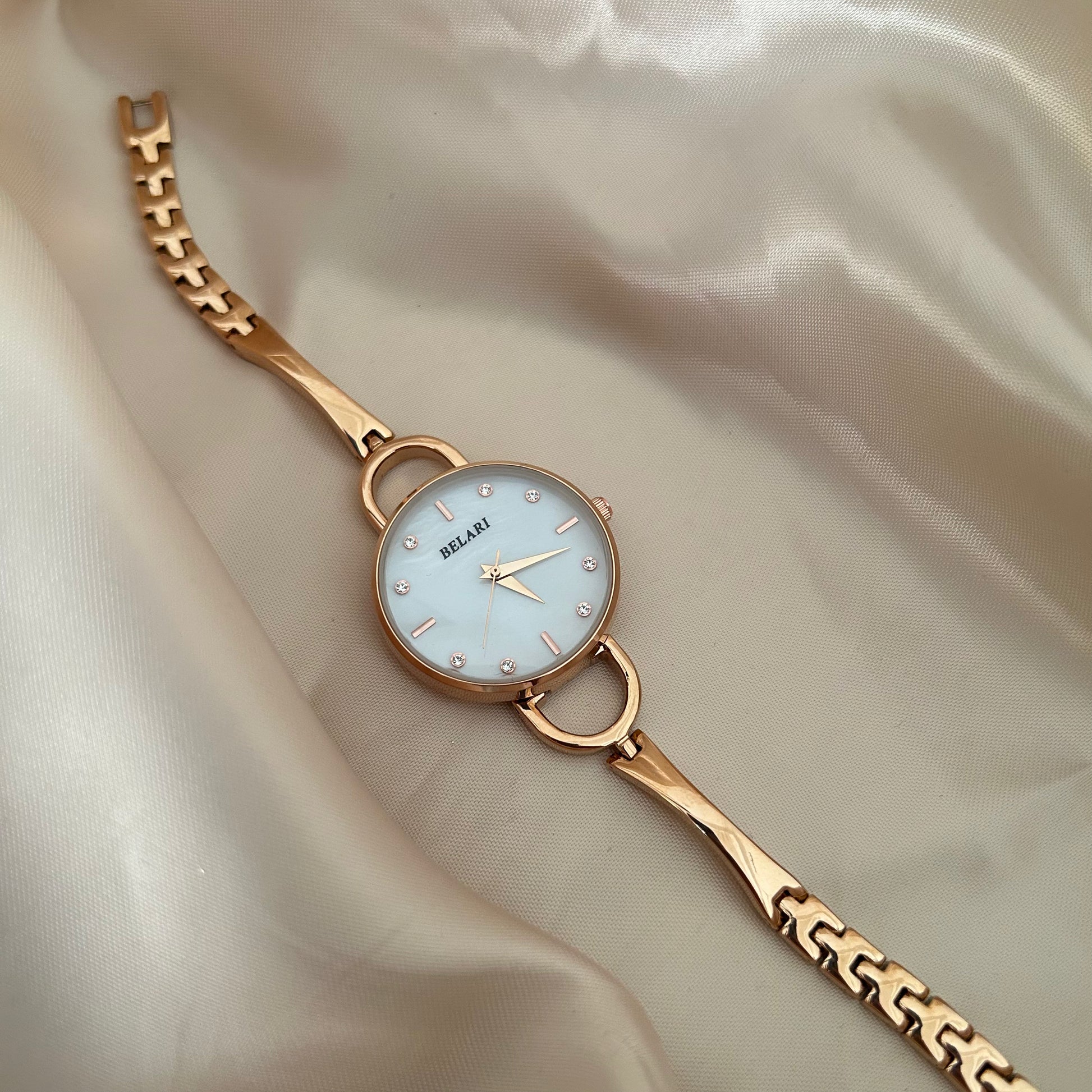 Slim gold wristwatch with loop connectors and small dial on beige satin background.