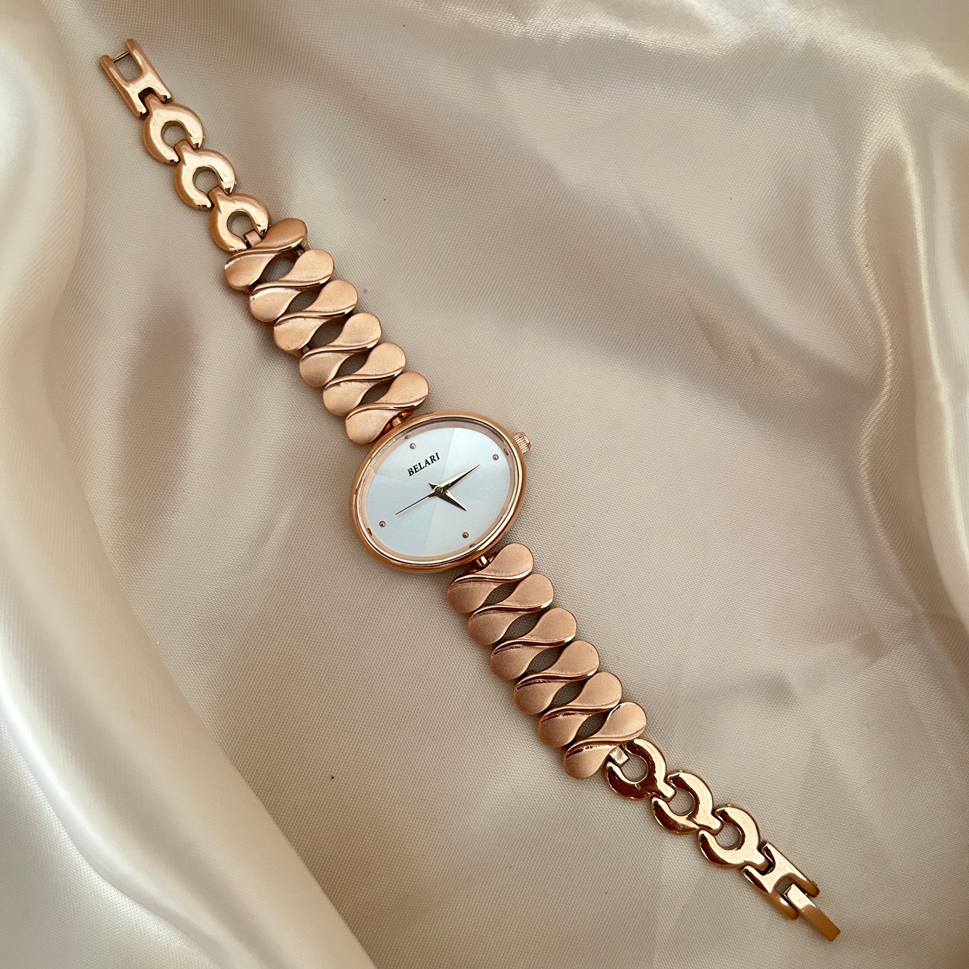 gold wristwatch with chain style bracelet and round dial placed on satin cloth.