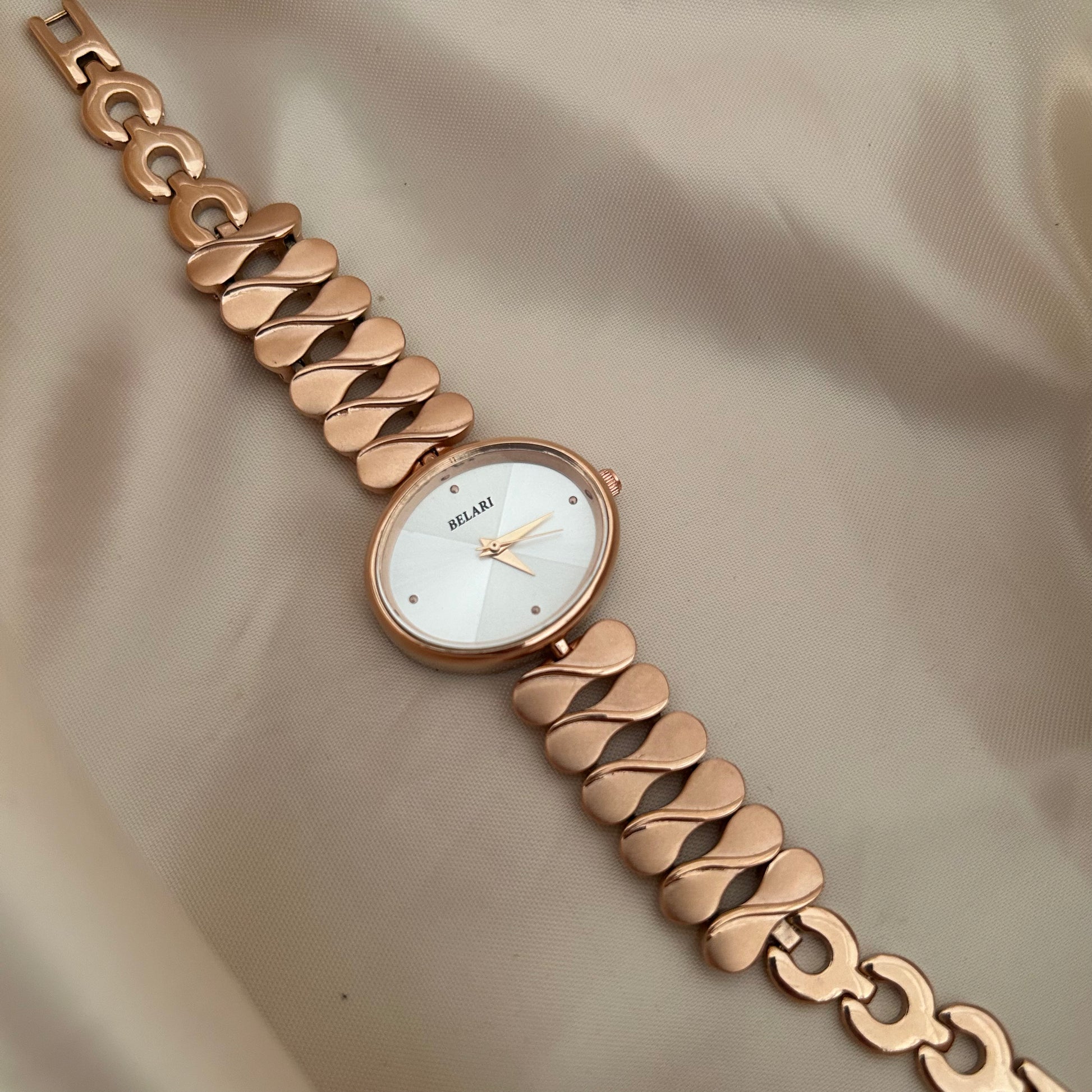 gold wristwatch with chain style bracelet and round dial placed on satin cloth.