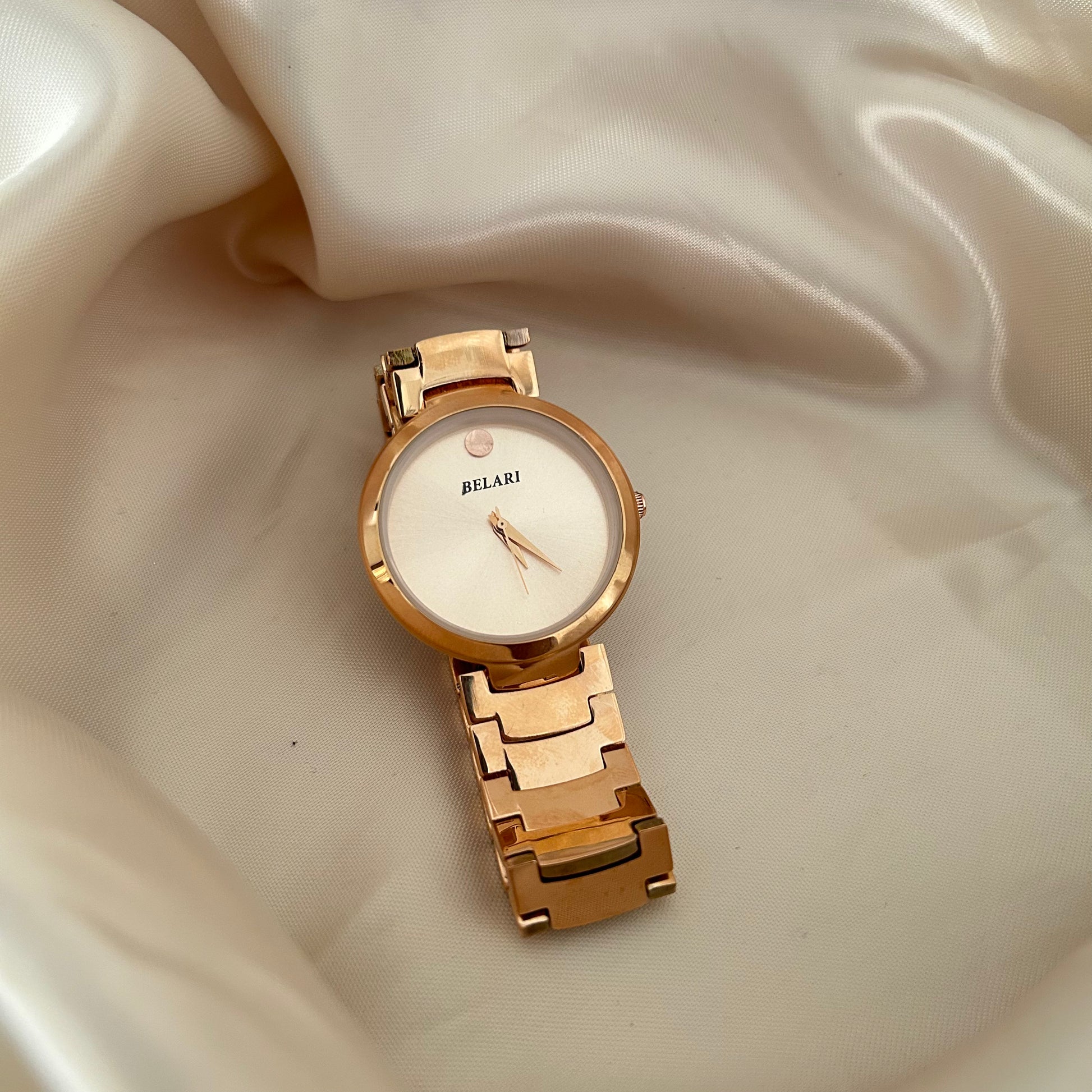 Minimal rose gold watch with plain dial and metal strap on soft fabric background.