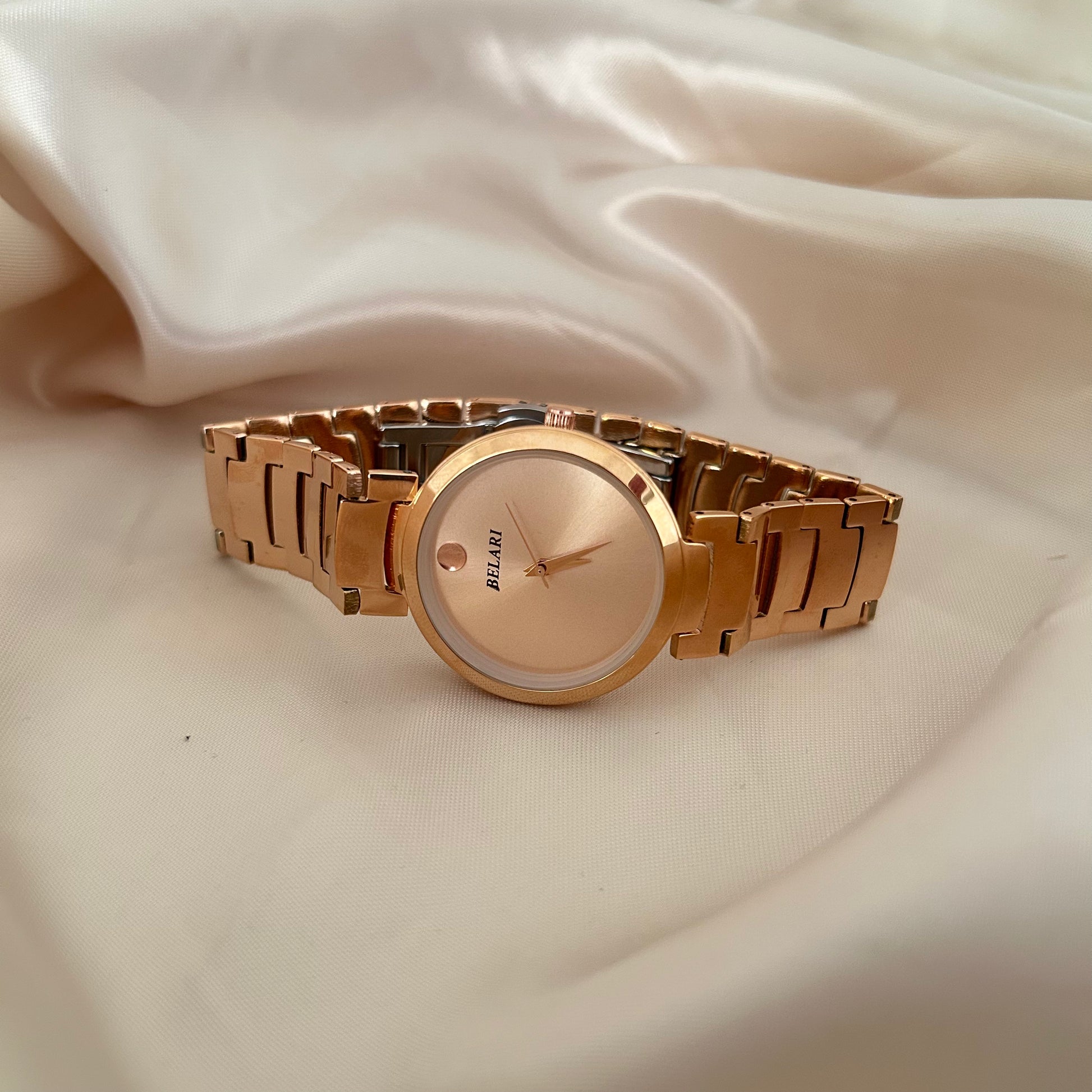 Minimal rose gold watch with plain dial and metal strap on soft fabric background.
