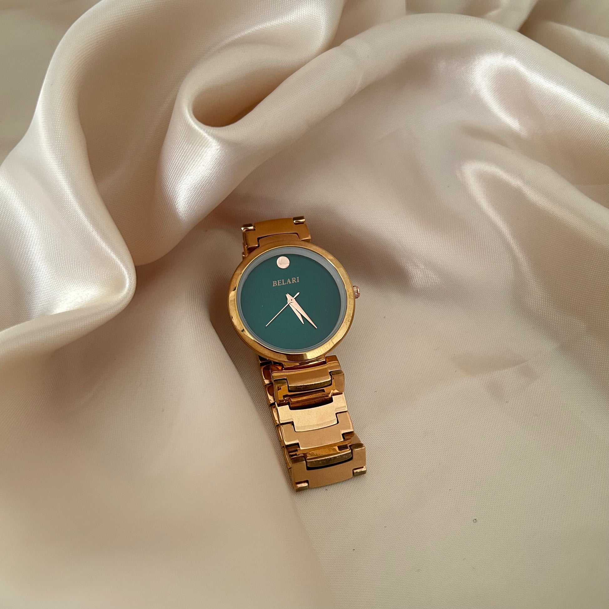 Minimal rose gold watch with plain dial and metal strap on soft fabric background.