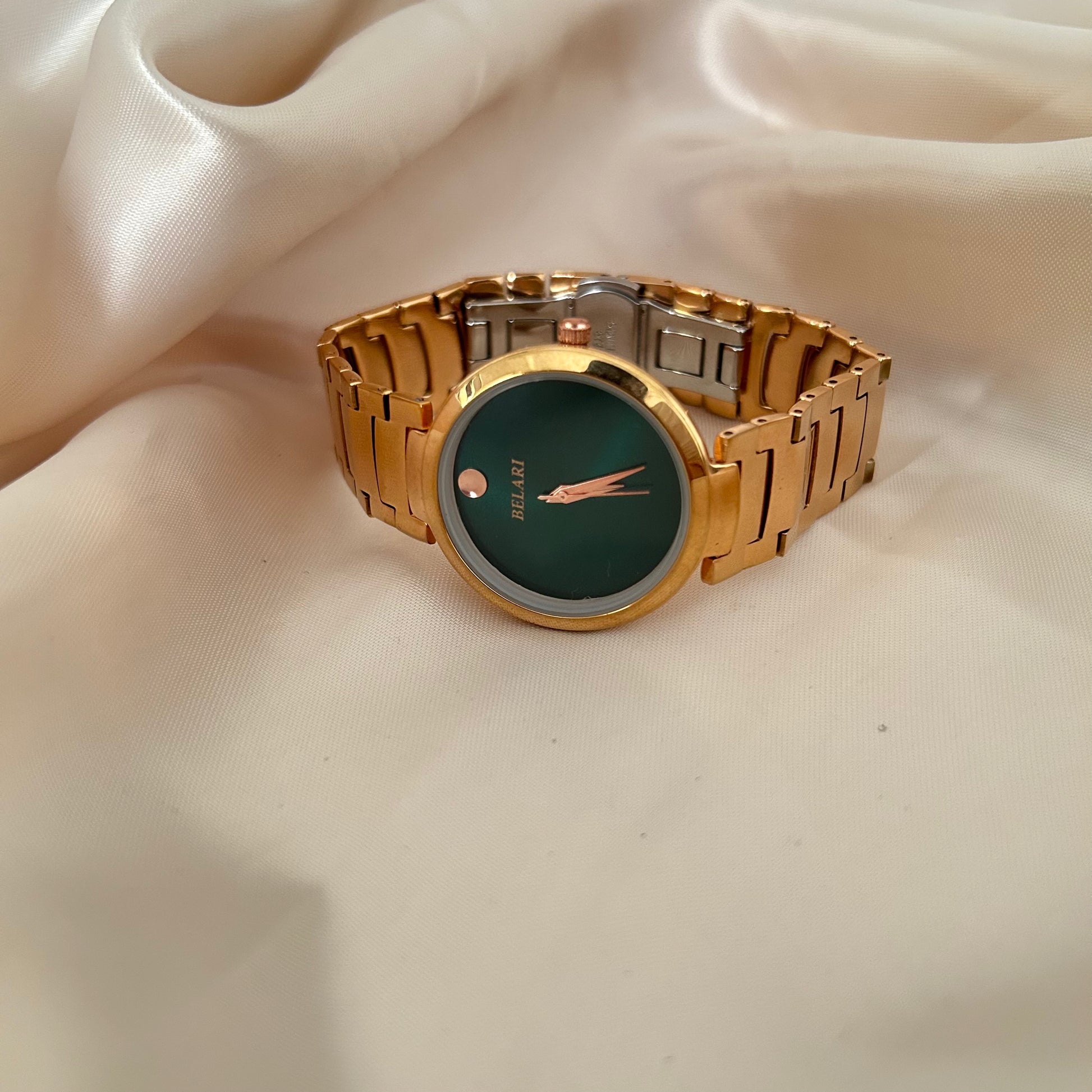 Minimal rose gold watch with plain dial and metal strap on soft fabric background.