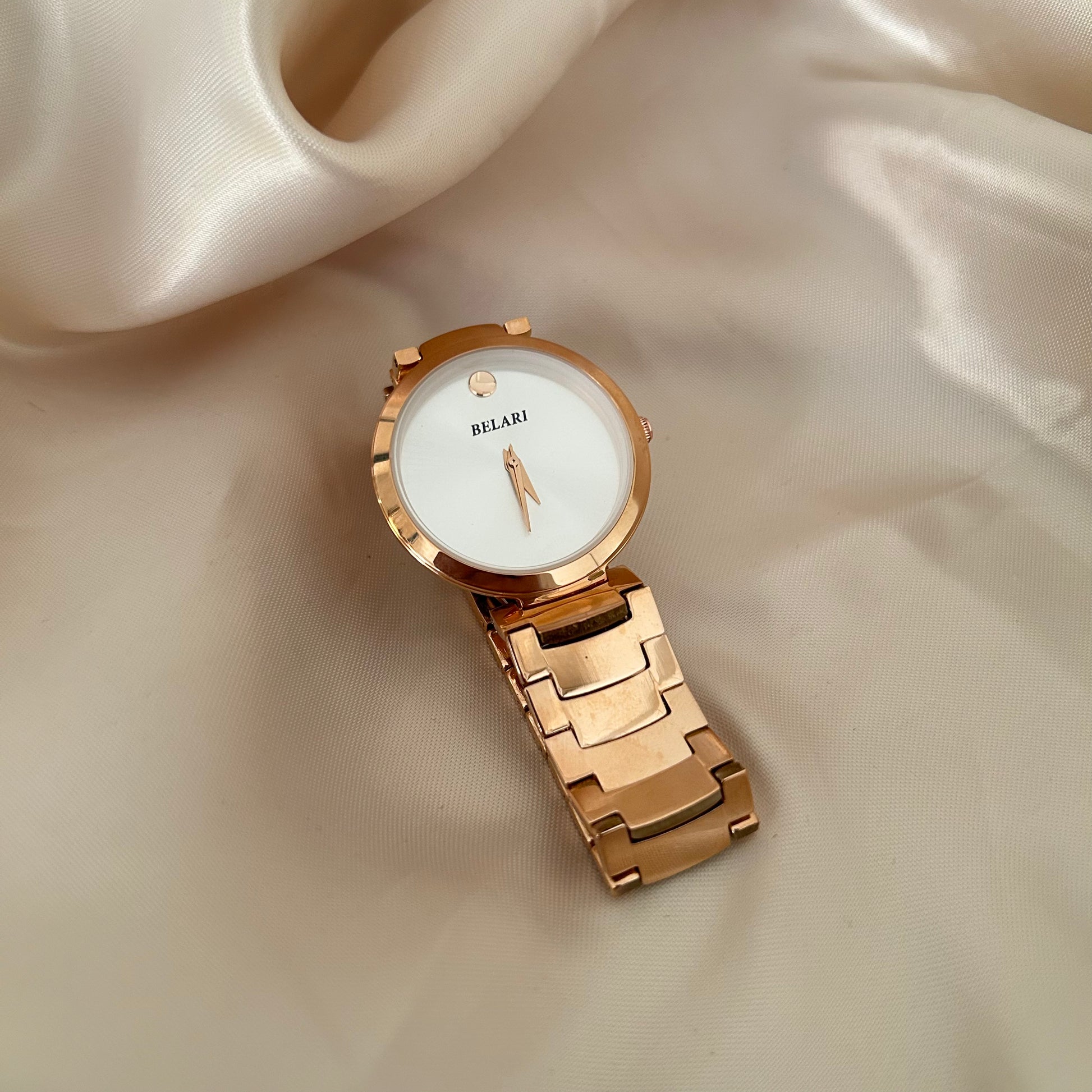Minimal rose gold watch with plain dial and metal strap on soft fabric background.
