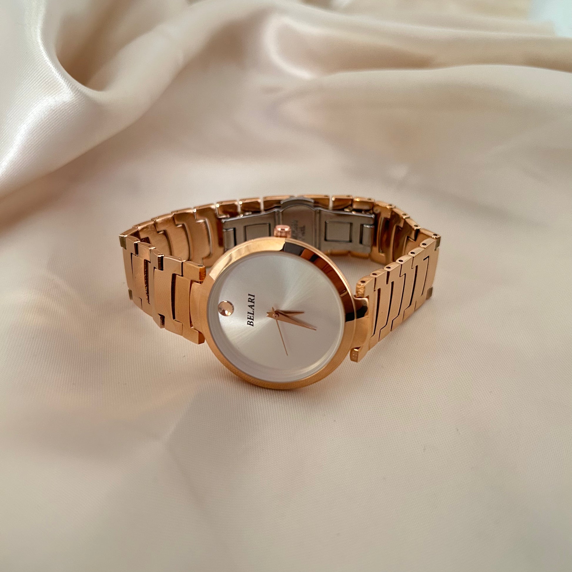 Minimal rose gold watch with plain dial and metal strap on soft fabric background.