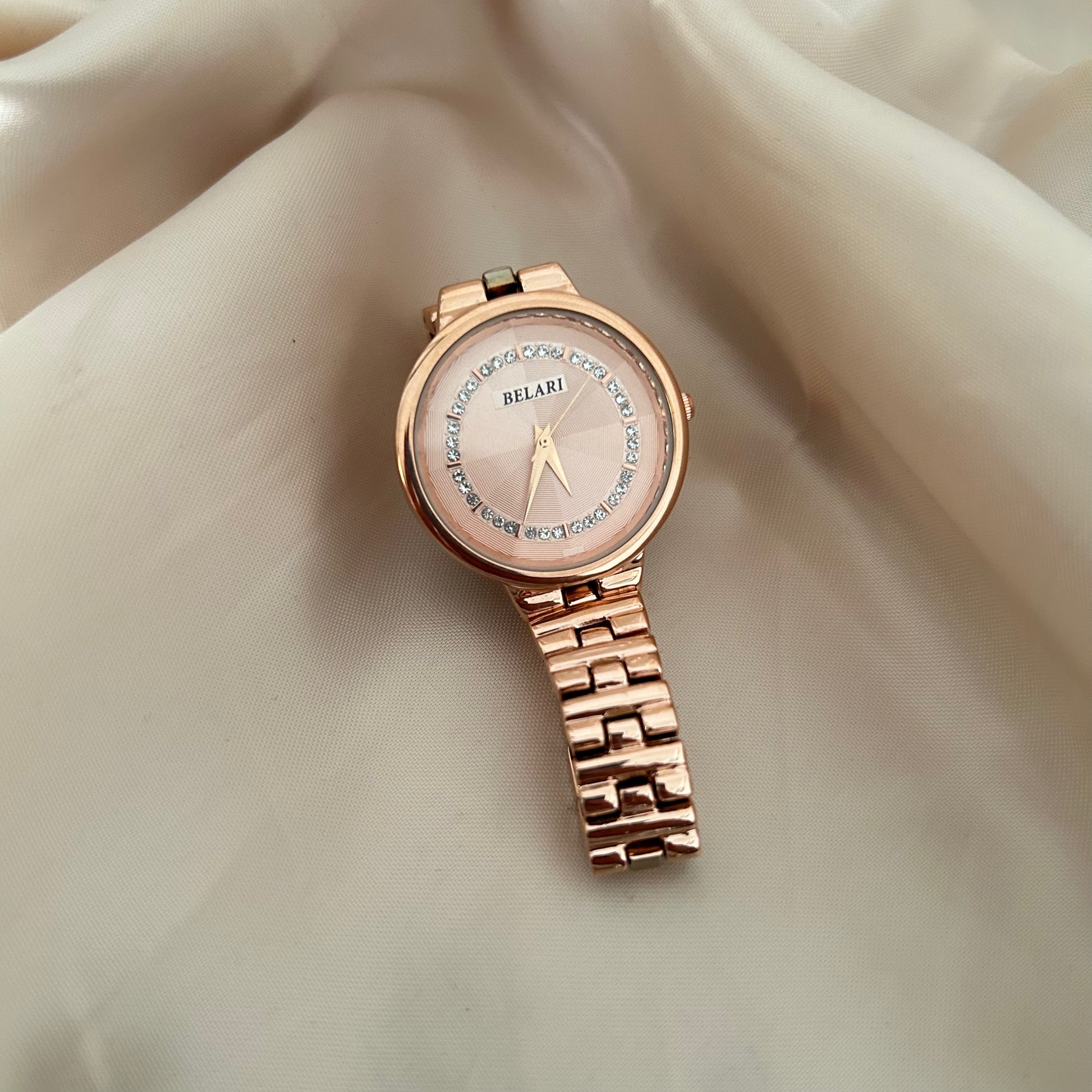 Rose gold wristwatch with crystal bezel and round dial placed on satin background.
