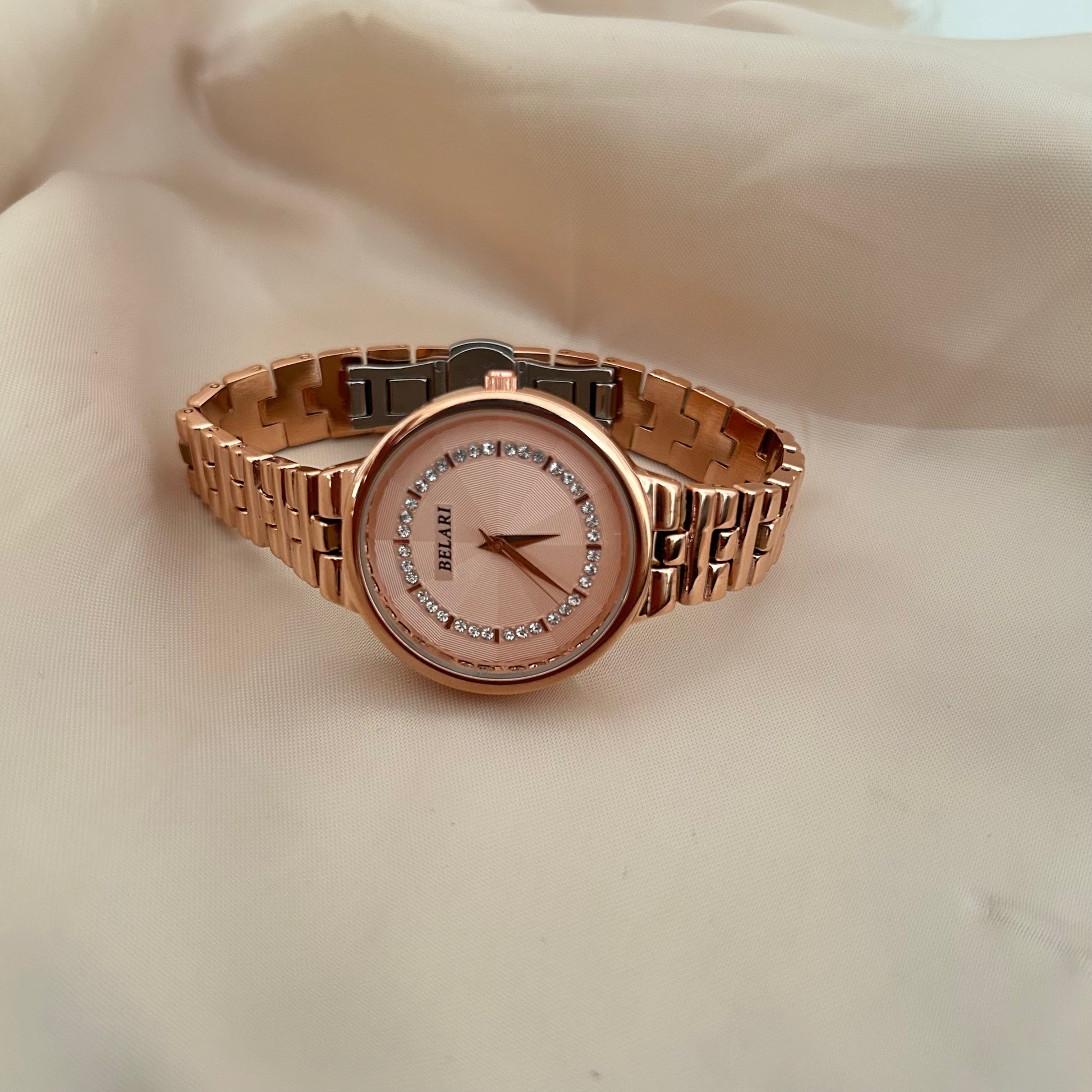 Rose gold wristwatch with crystal bezel and round dial placed on satin background.
