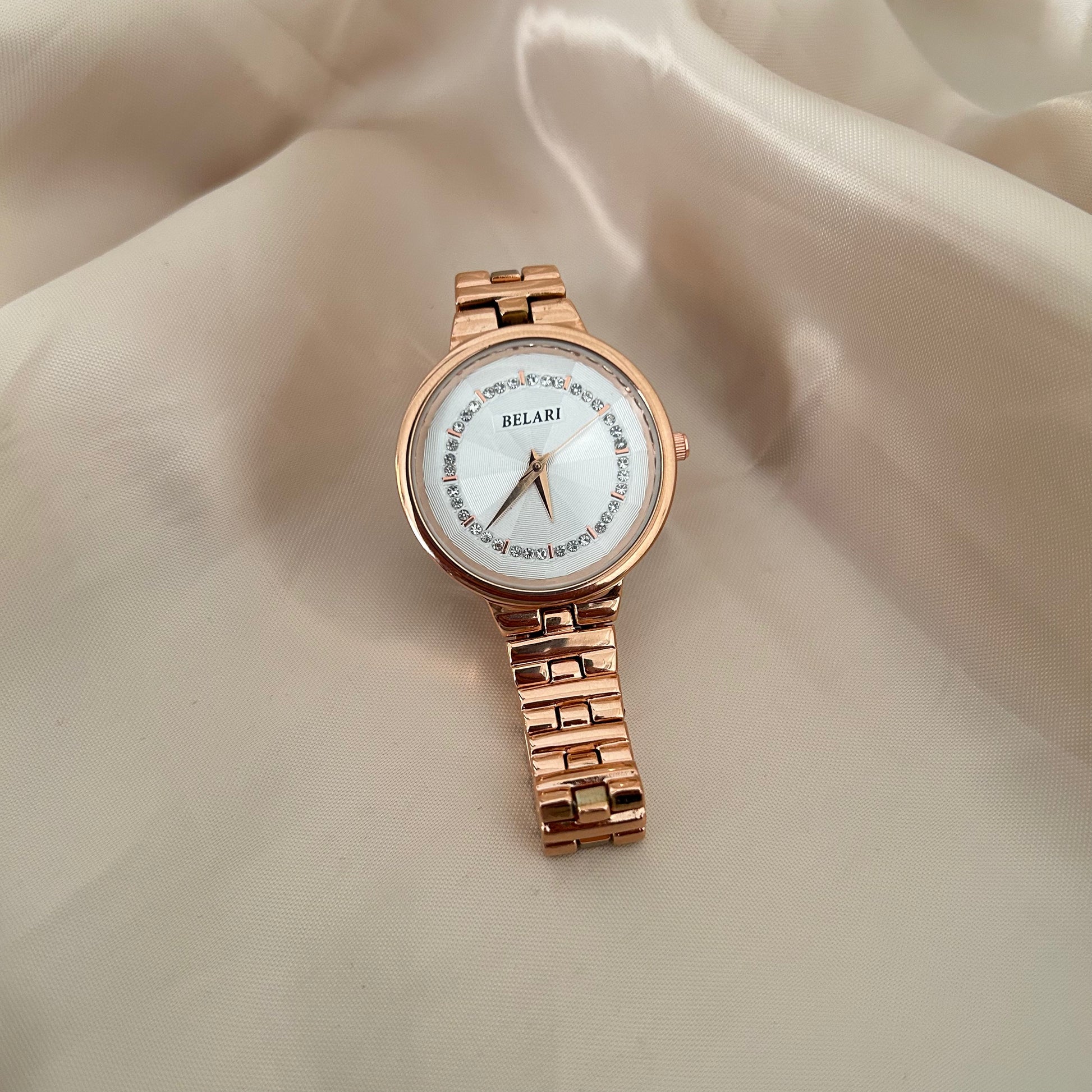 Rose gold wristwatch with crystal bezel and round dial placed on satin background.