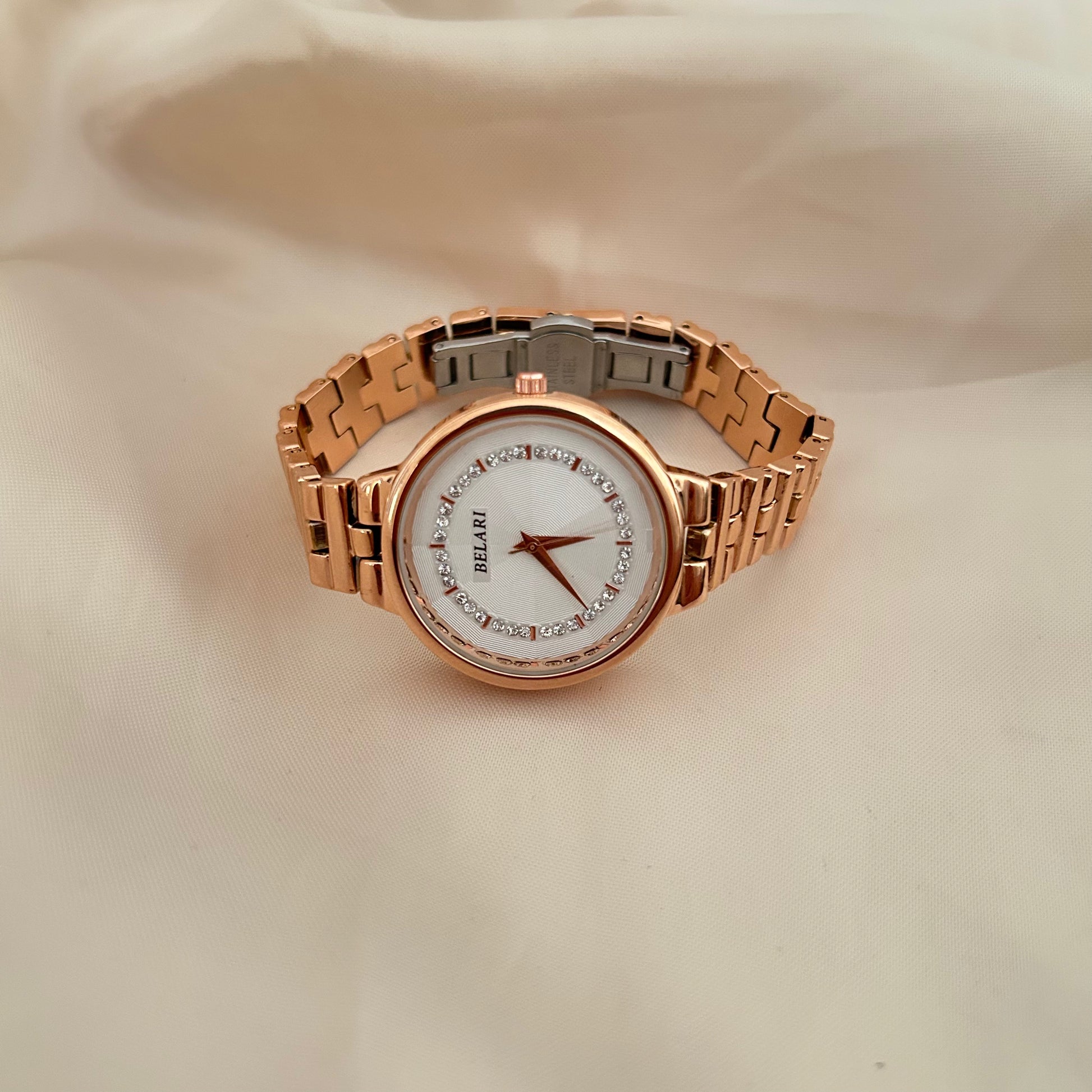 Rose gold wristwatch with crystal bezel and round dial placed on satin background.