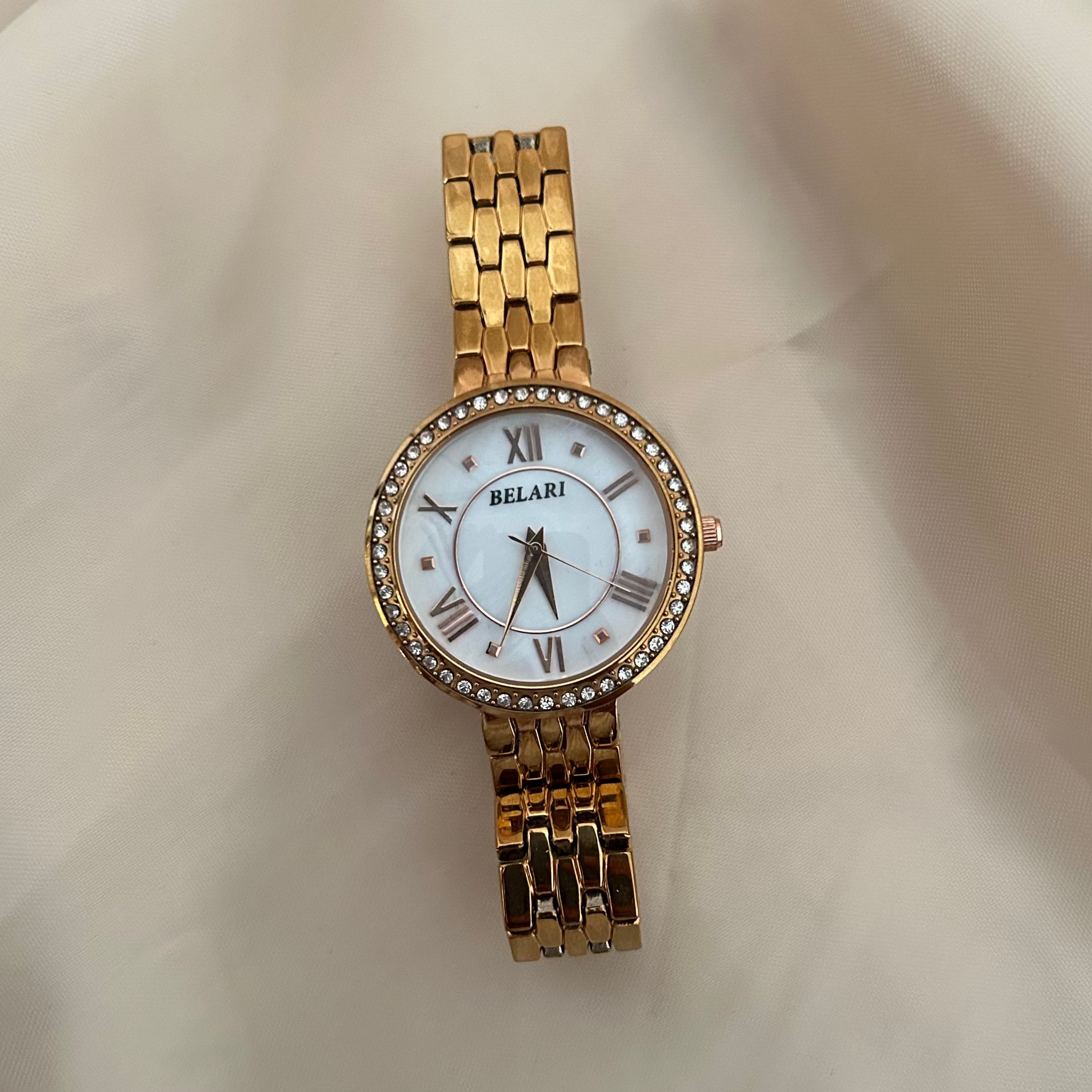 White wristwatch with Roman numeral dial and crystal studded bezel on soft satin background.