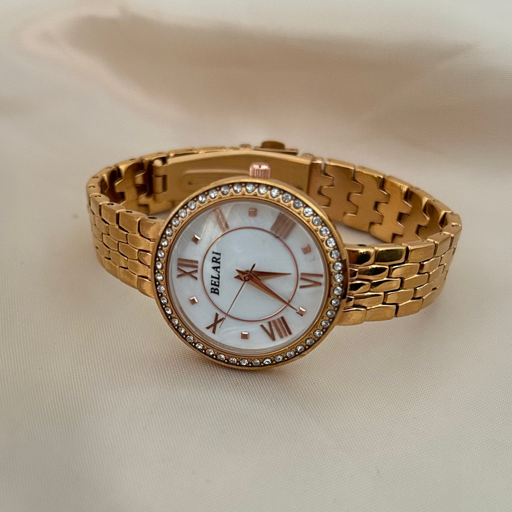 White wristwatch with Roman numeral dial and crystal studded bezel on soft satin background.