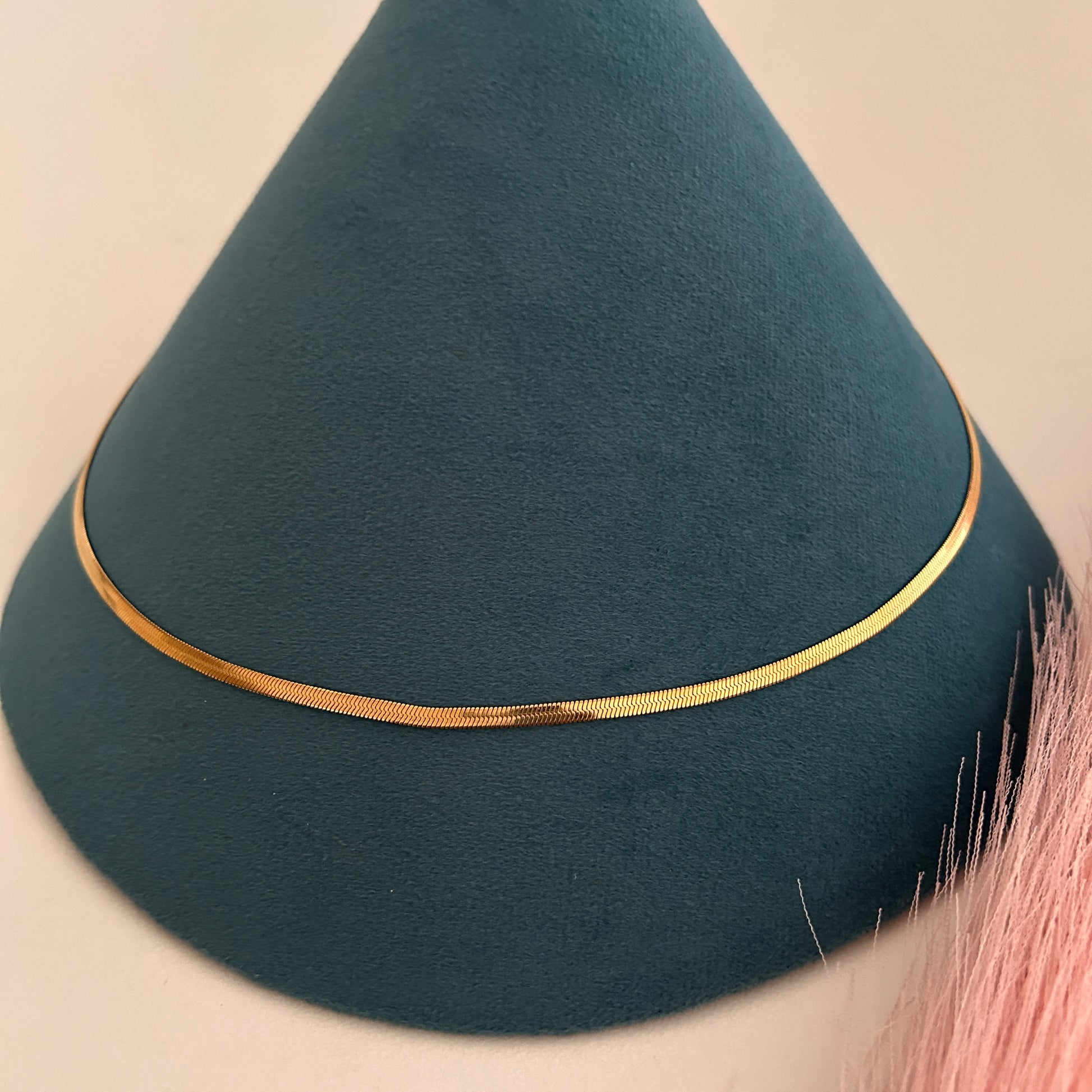 Flat herringbone gold waist band with smooth polished surface on teal display.