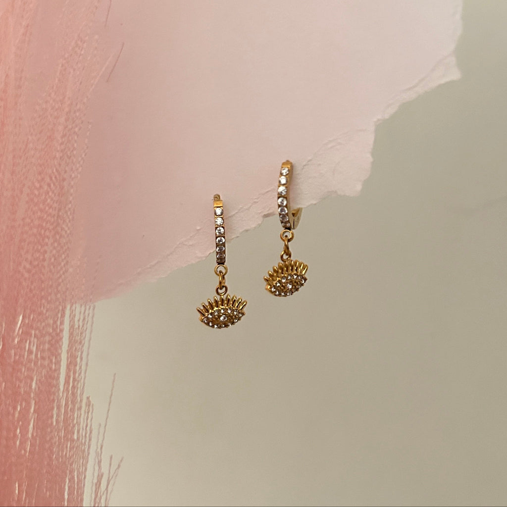 Gold hoop earrings with crystal detailing and eye-shaped dangling charms.