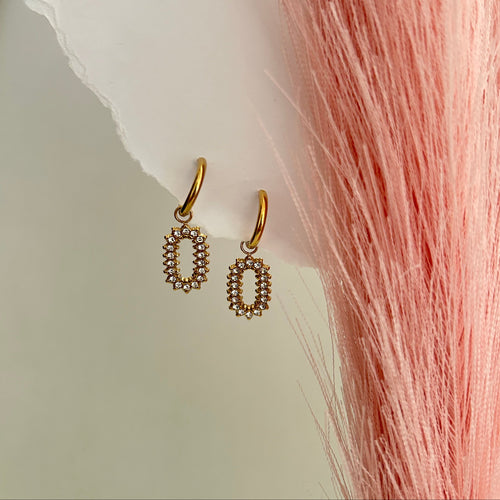 Gold oval drop earrings with small crystal stones arranged in a halo pattern, hanging from delicate gold hoops on a soft neutral background.