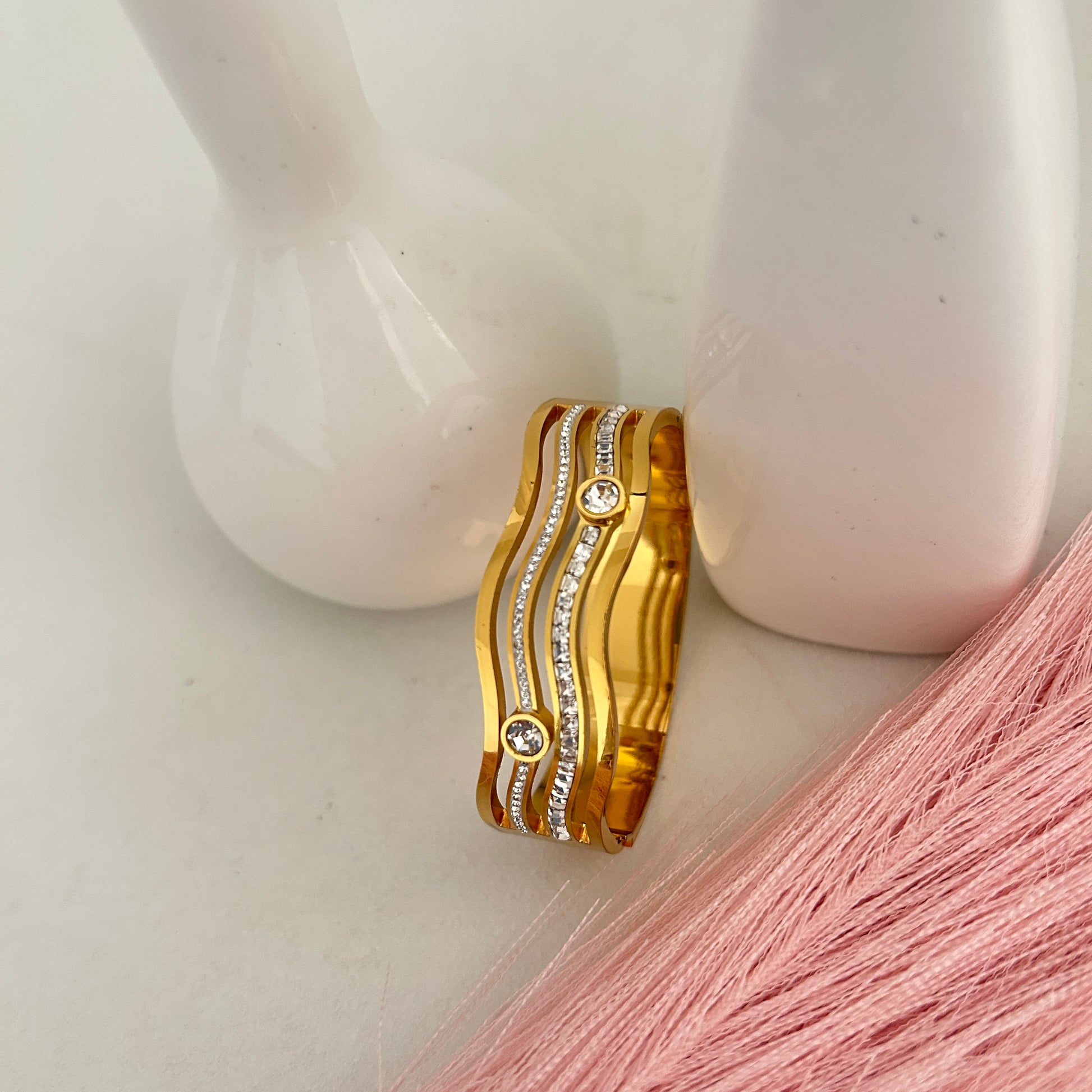 Gold wavy bangle bracelet with crystal accents placed near white decor.
