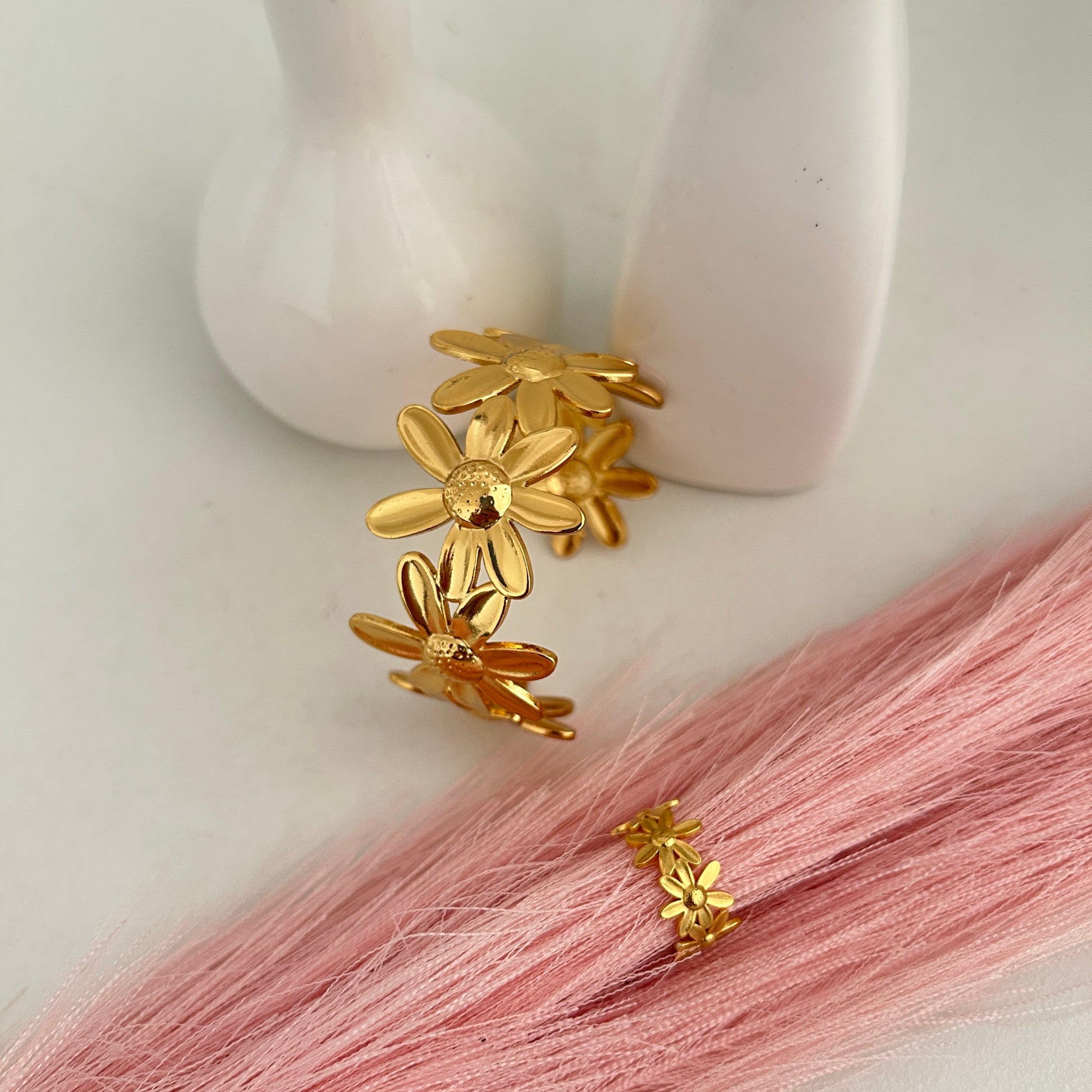 Gold daisy flower cuff bracelet with matching ring on pink background.