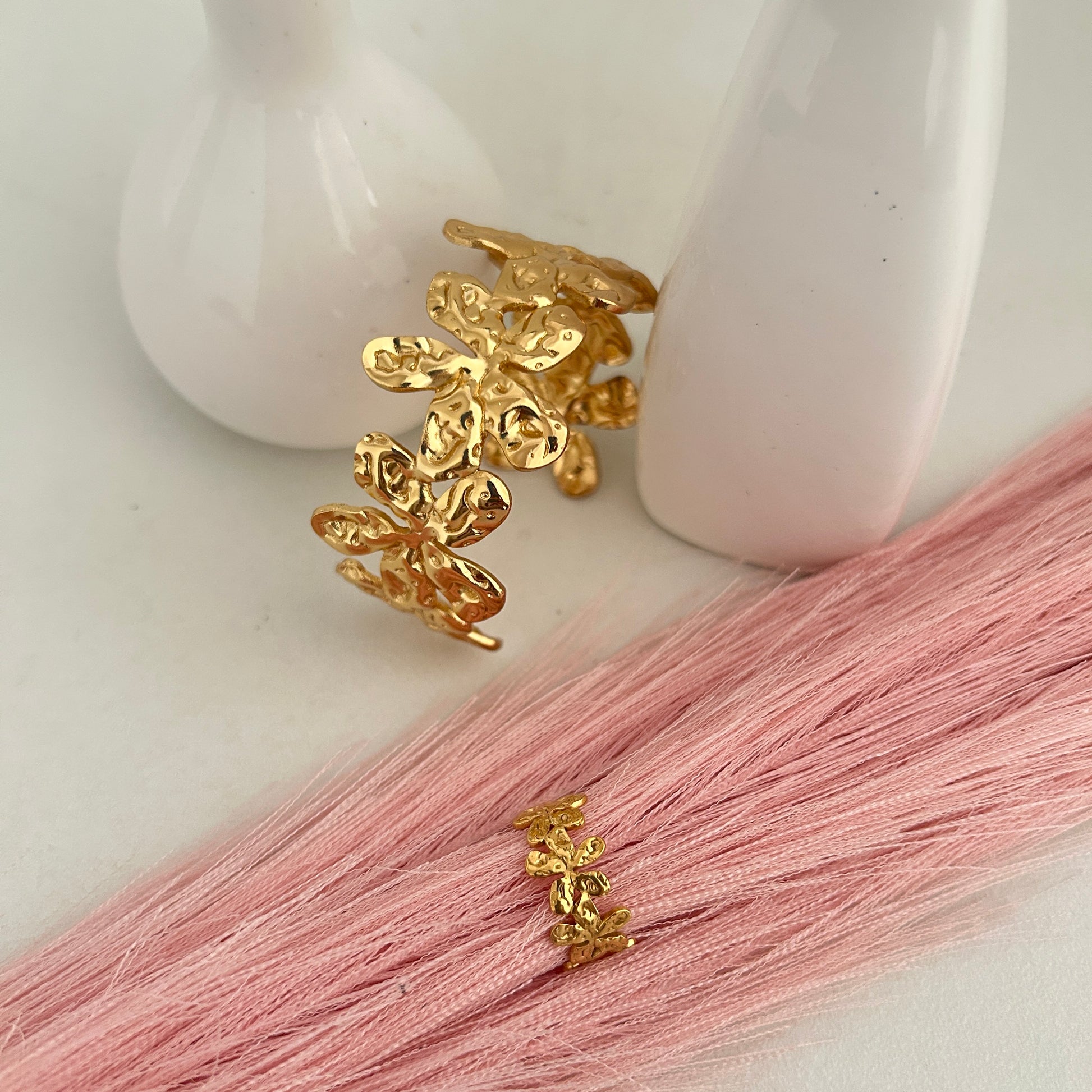 Gold floral open cuff bracelet with matching flower ring on pink background.