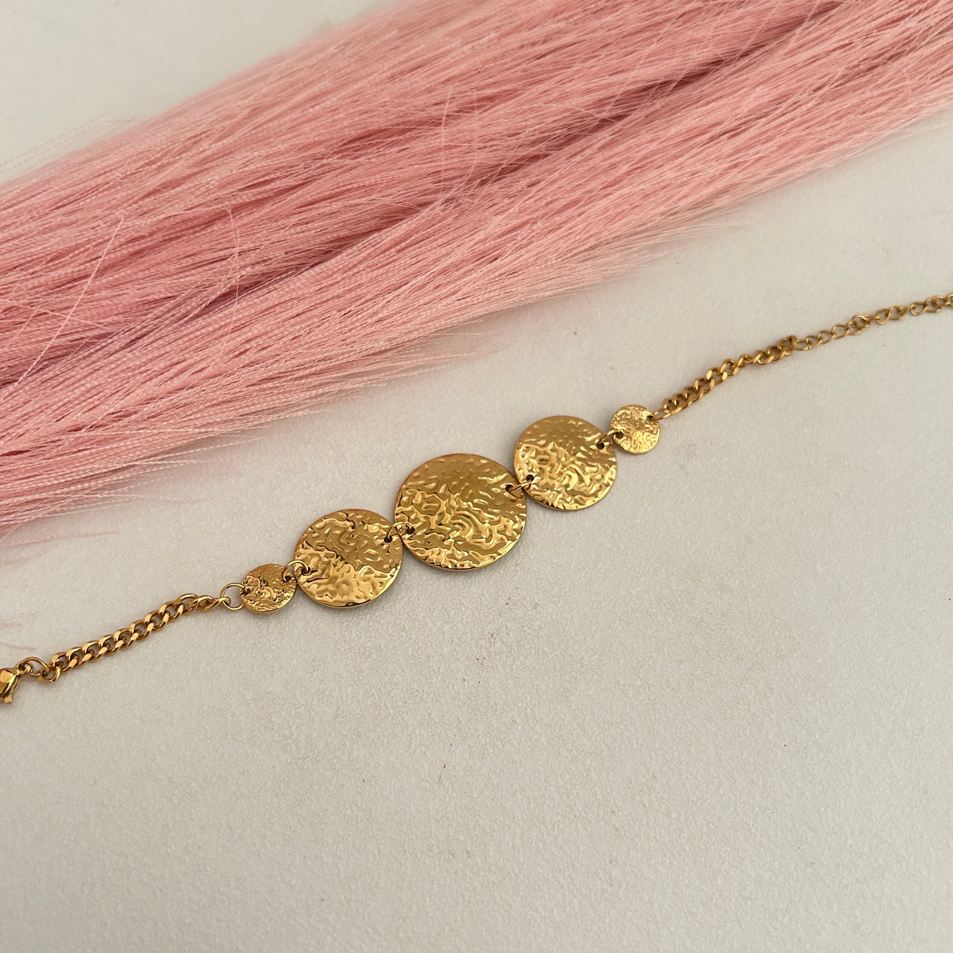 Gold hammered disc chain bracelet on soft pink surface.